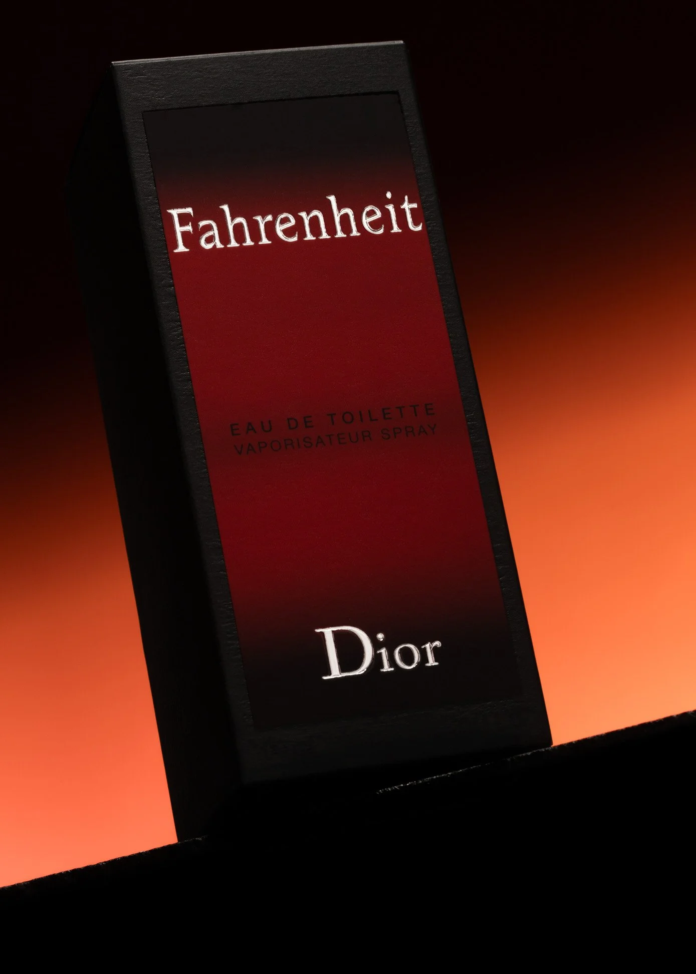 A black box of Dior Fahrenheit Eau de Toilette spray with a gradient red and black label, set against a dark, gradient background.