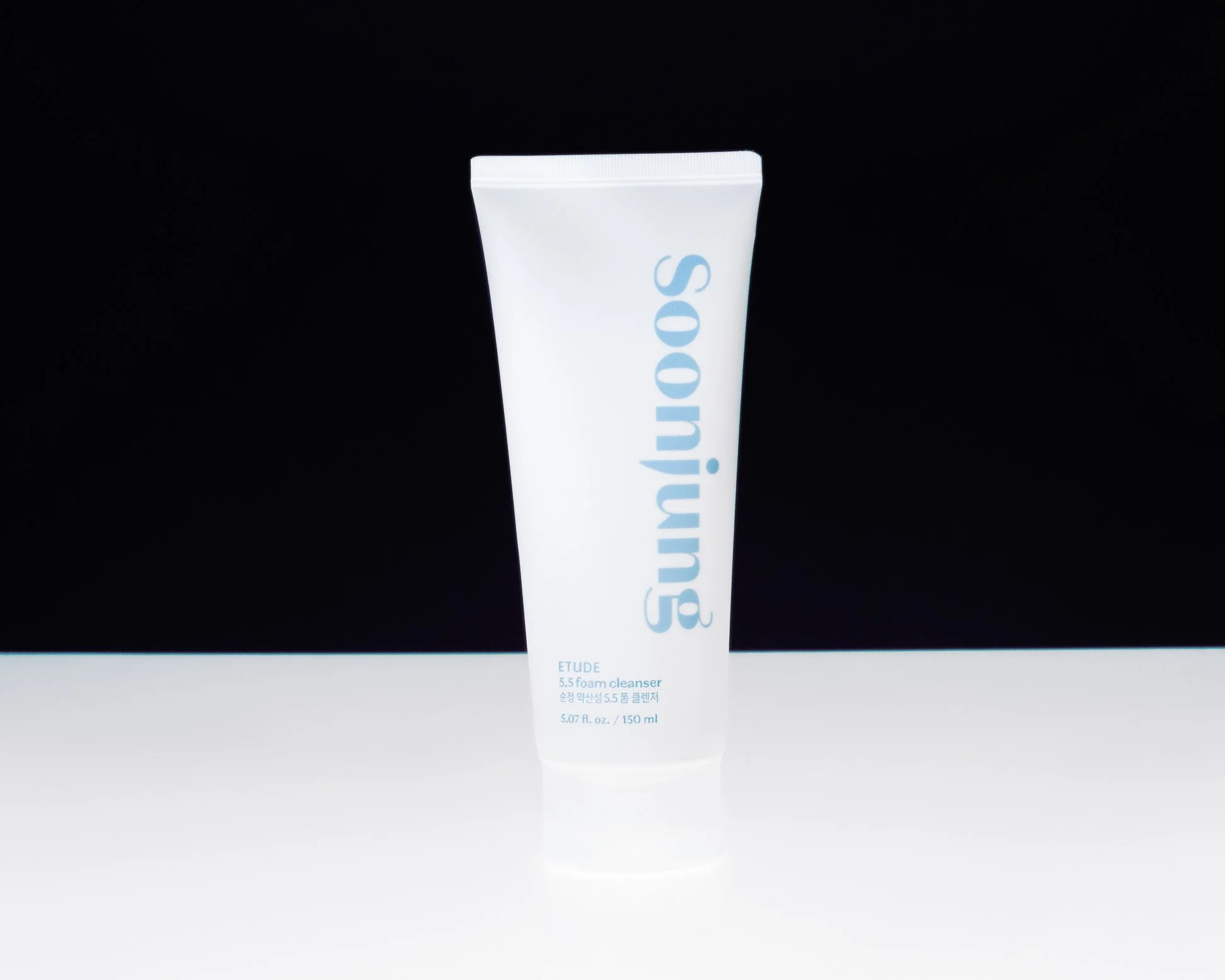 A white tube of ETUDE foam cleanser with blue text on a white surface against a black background.