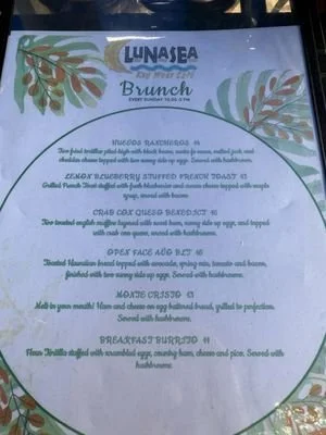 Menu listing breakfast dishes with a decorative leafy border, including mixed breakfast, eggs Florentine, crab cake Benedict, open face EGG, breakfast Burrito, and breakfast skillet, with descriptions and ingredients.