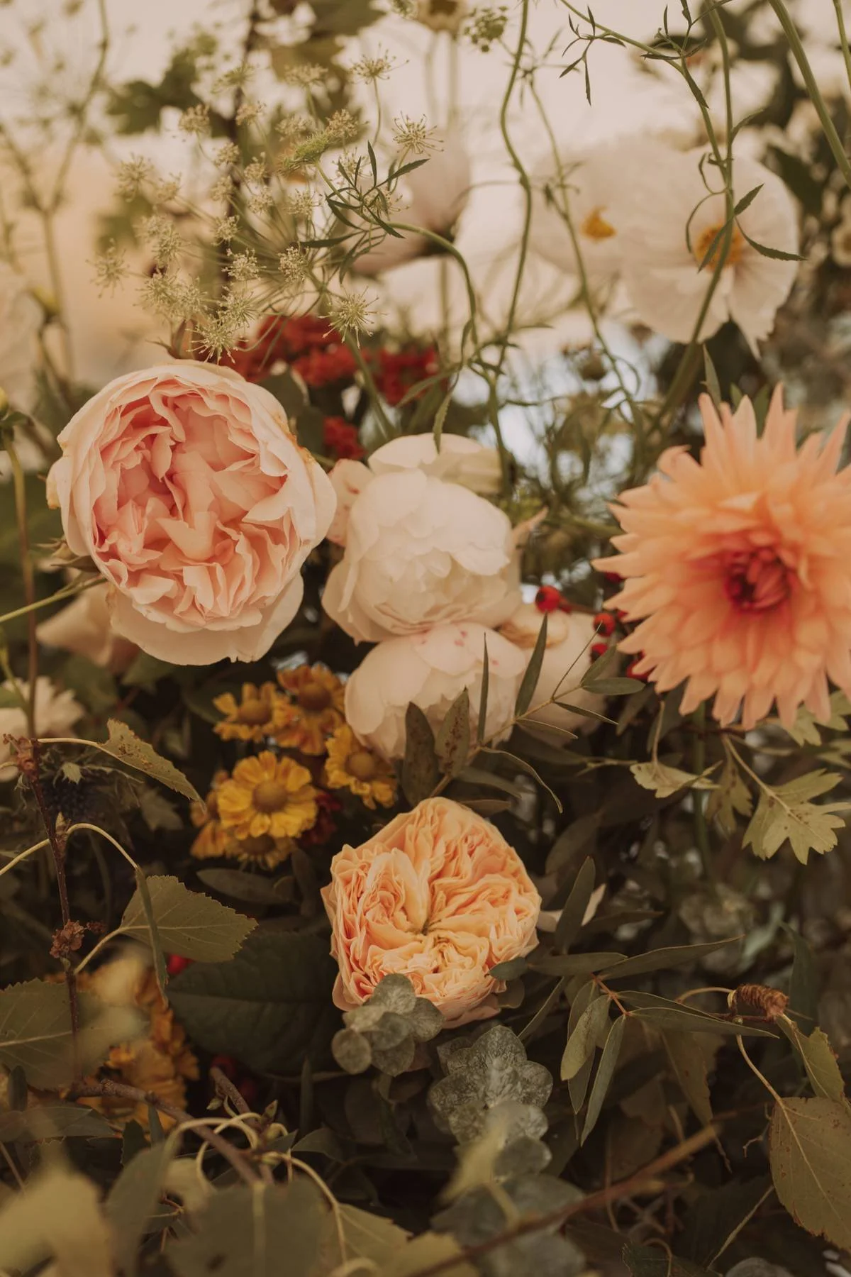 A close-up photo of a bouquet with pink and white peonies, yellow small flowers, and greenery.