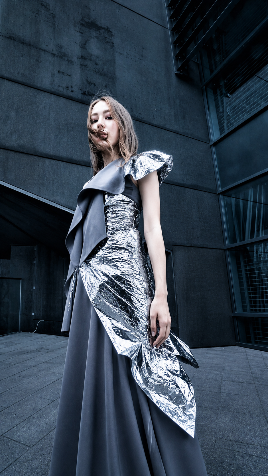 Model wearing a sculptural silver and grey dress against modern architecture in the Novality project by Krys Kona