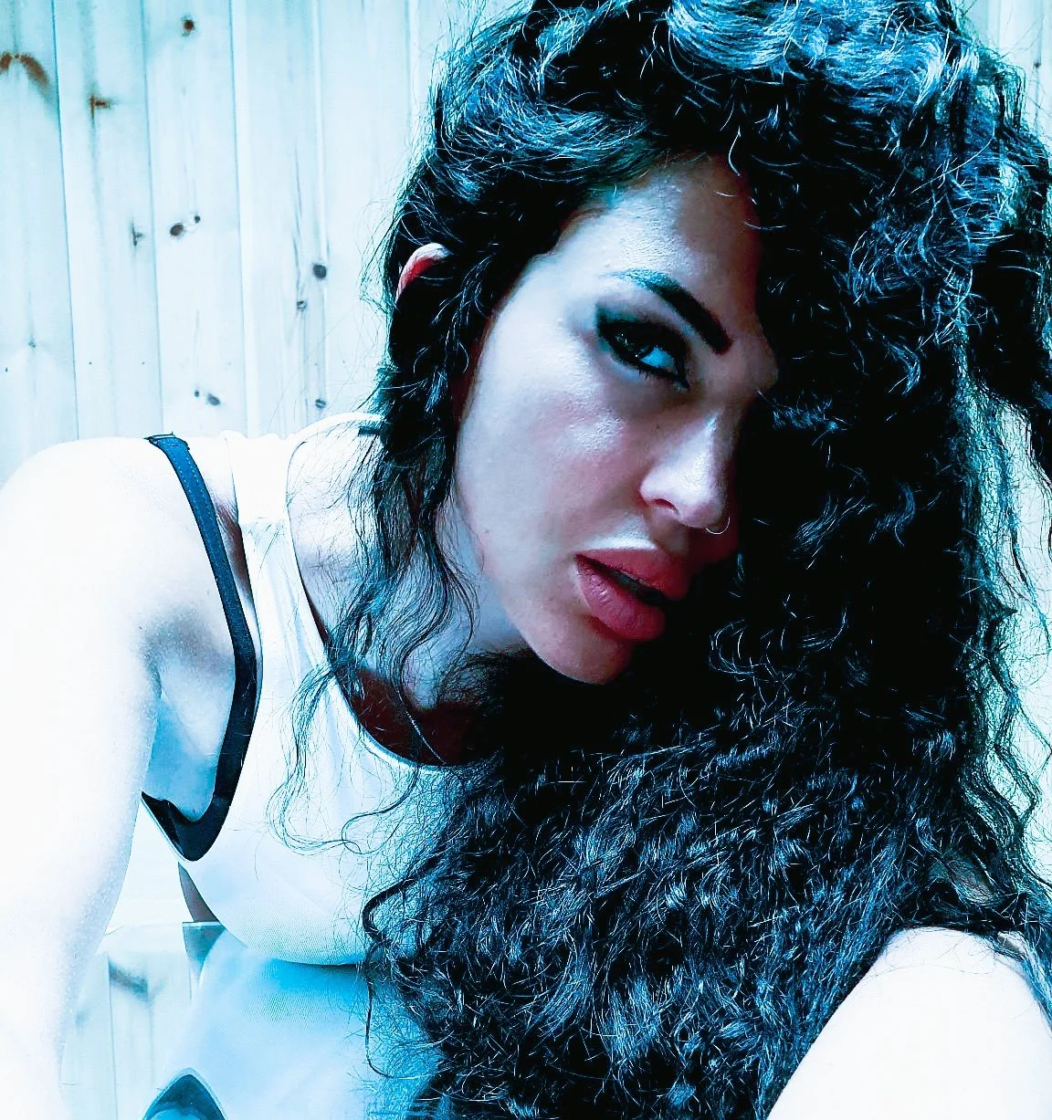Close-up portrait of a woman with voluminous dark curls and pink lips under cool blue light, from Transformative by Krys Kona.