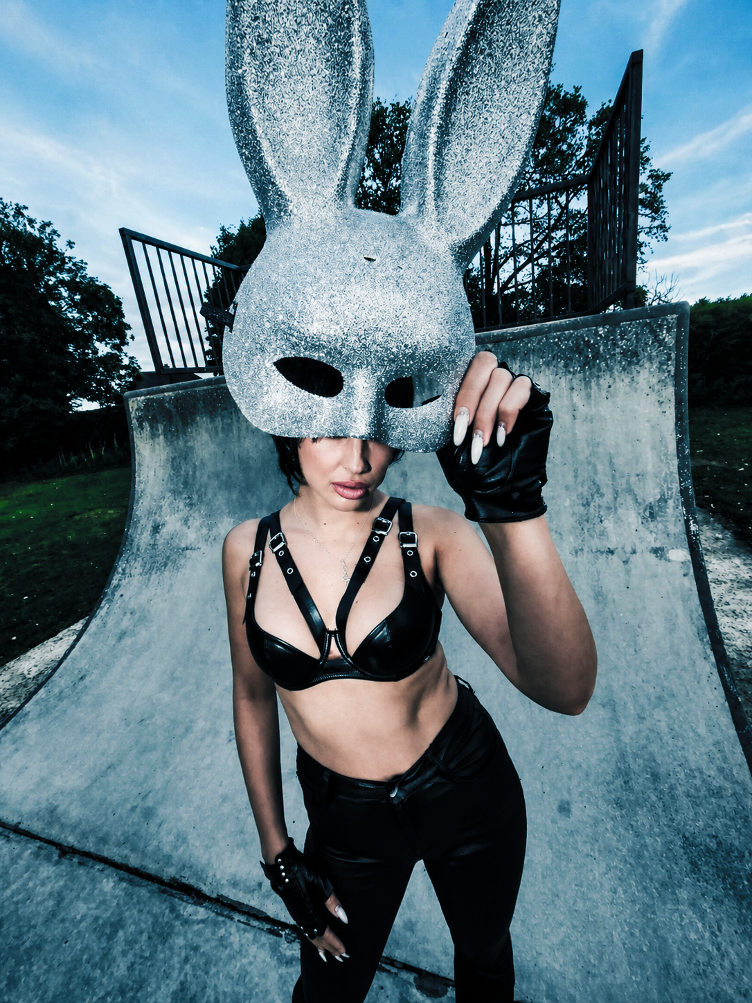 Fashion portrait of a woman wearing an oversized silver rabbit mask and black leather outfit in a concrete skatepark, part of the New Wave Project by Krys Kona.