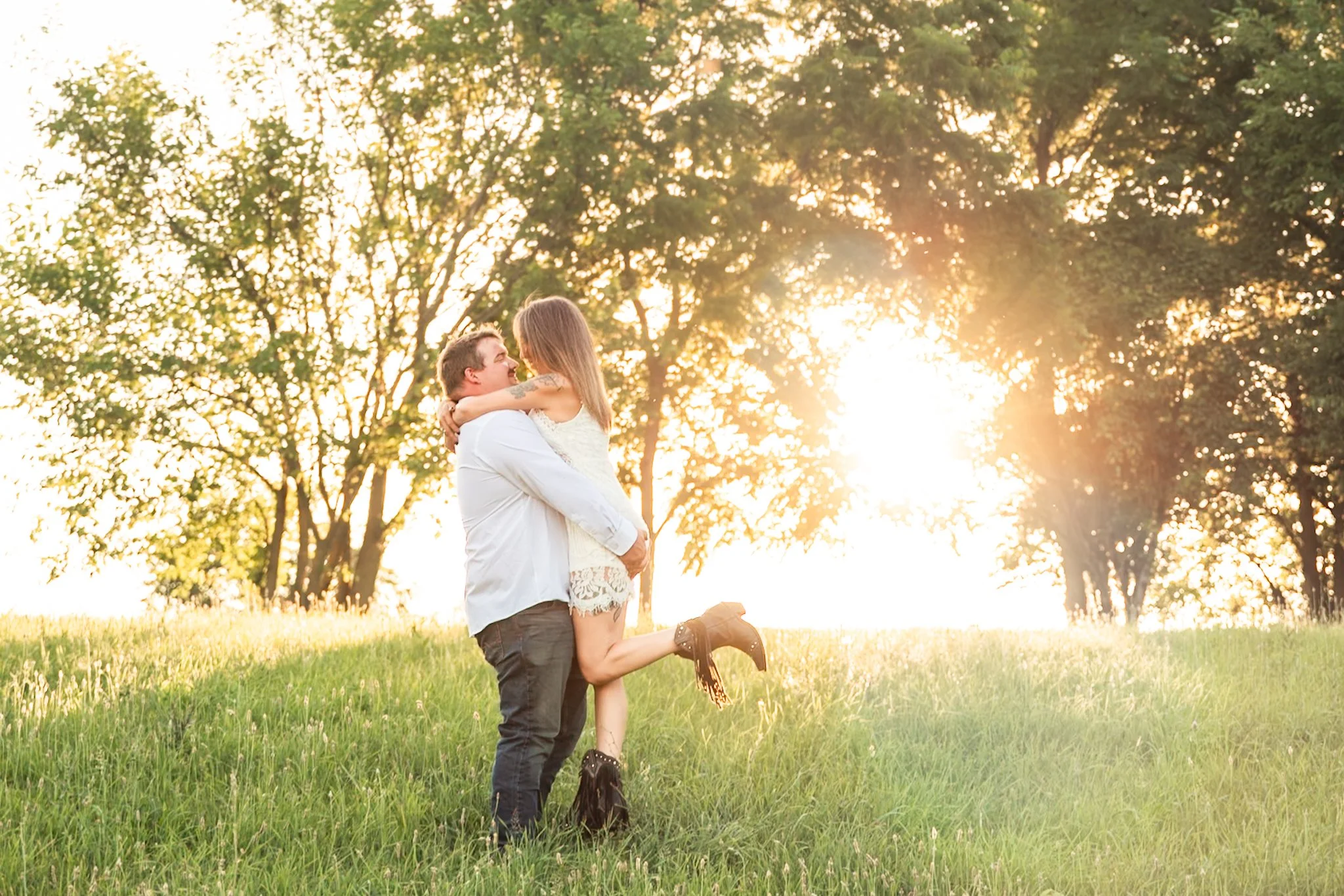 A couple in love, with the man lifting the woman in a grassy outdoor setting during sunset.