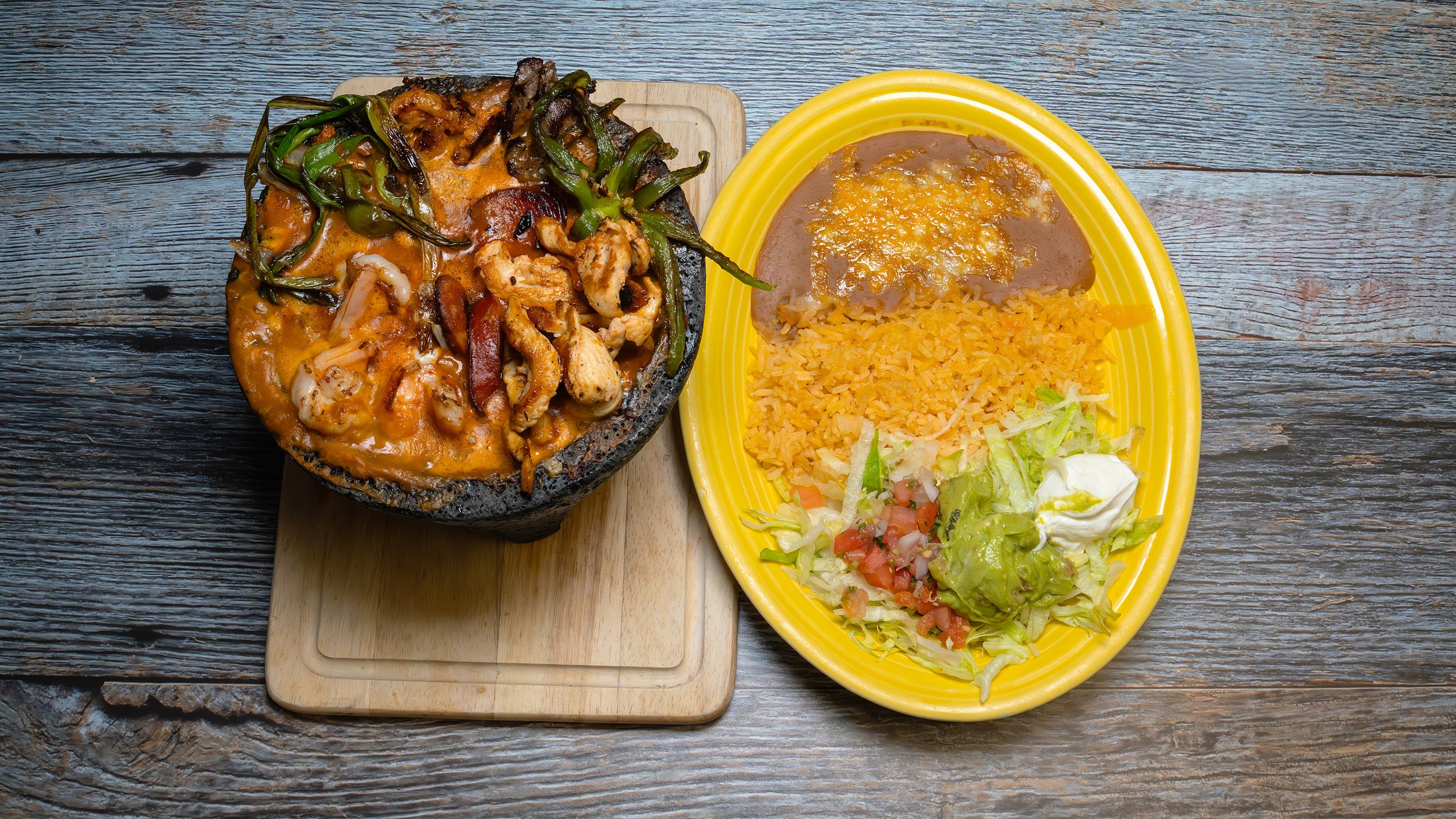 Delicious Mexican molcajete served sizzling hot, featuring a savory combination of meats, shrimp, chorizo, melted cheese, and green onions, all smothered in a flavorful homemade salsa. Served with rice, beans, and tortillas.