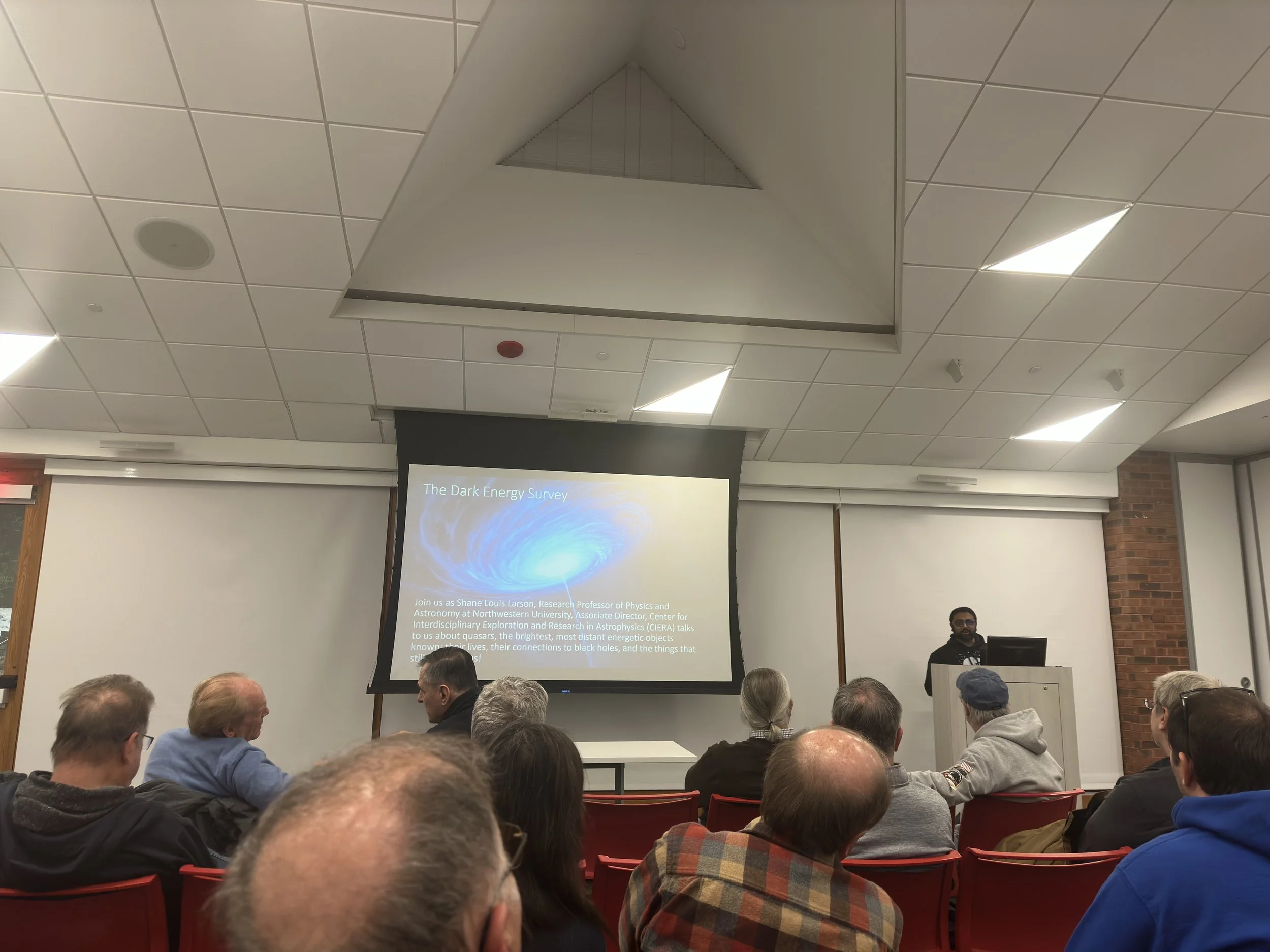 Audience listening to a presentation about the Dark Energy Survey in a lecture hall.