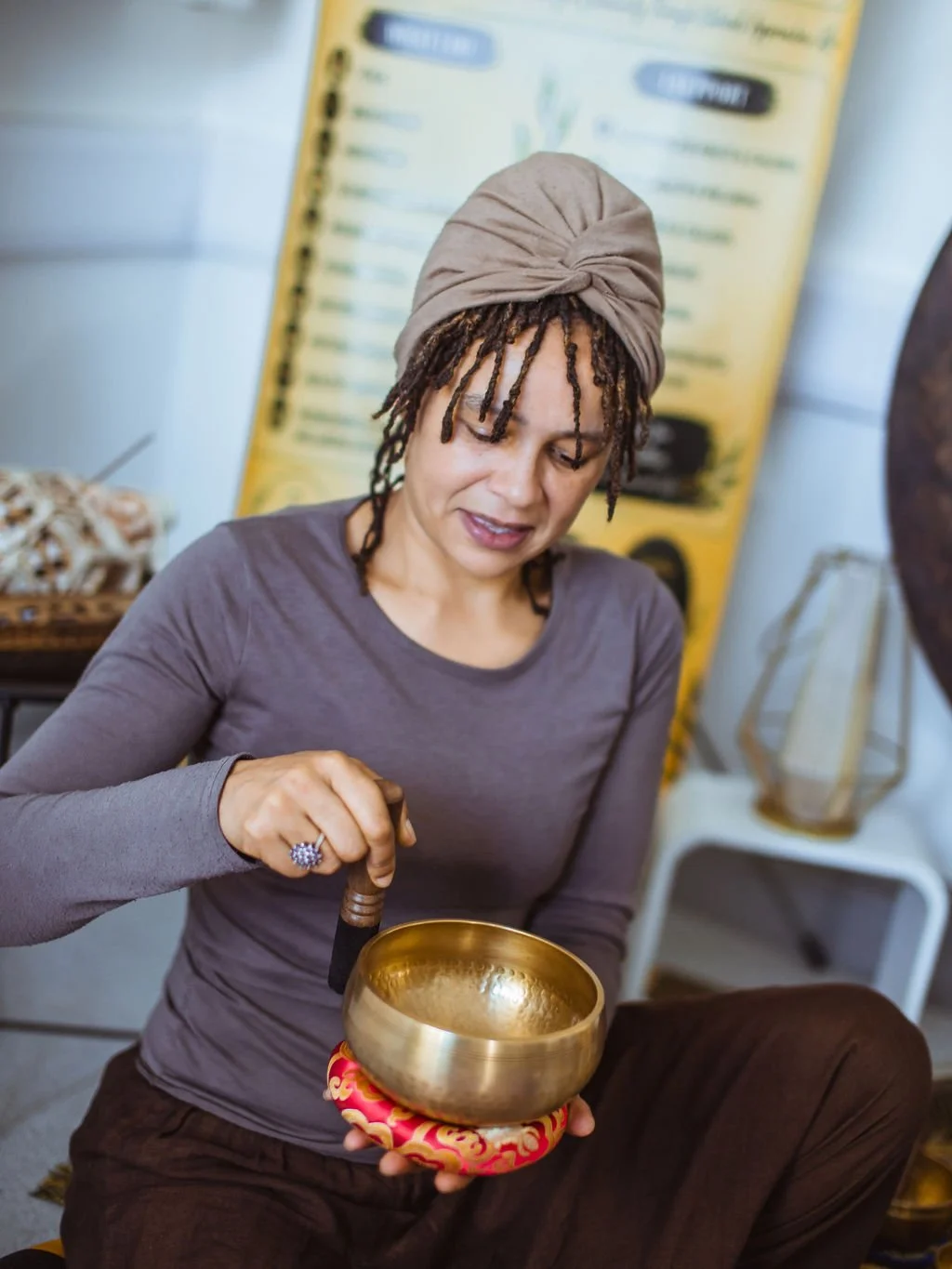 Woman holding and playing a brass singing bowl with a wooden mallet