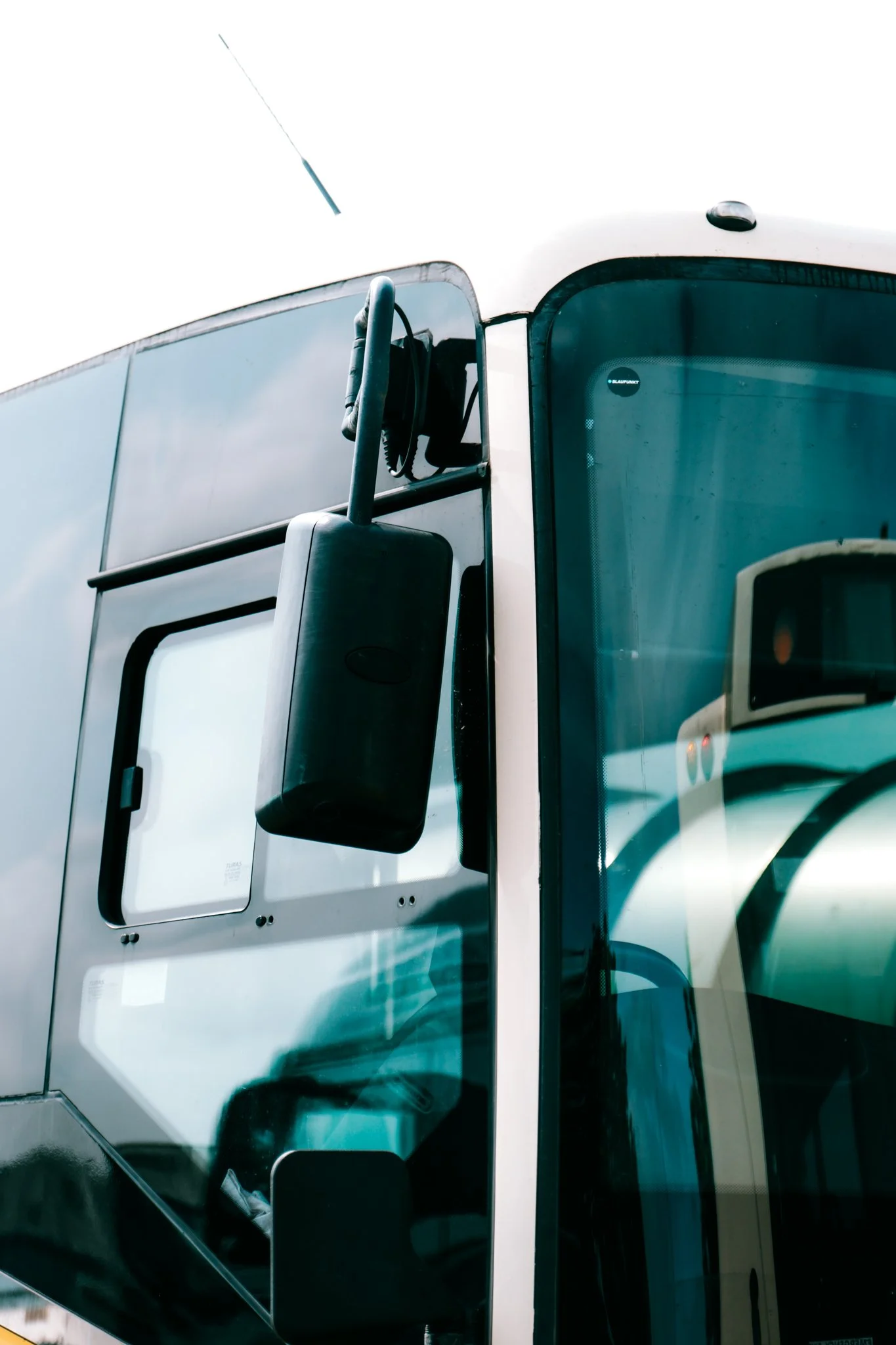 Close-up of the front section of a modern white semi-truck, showing the side mirror, windshield, and part of the cab