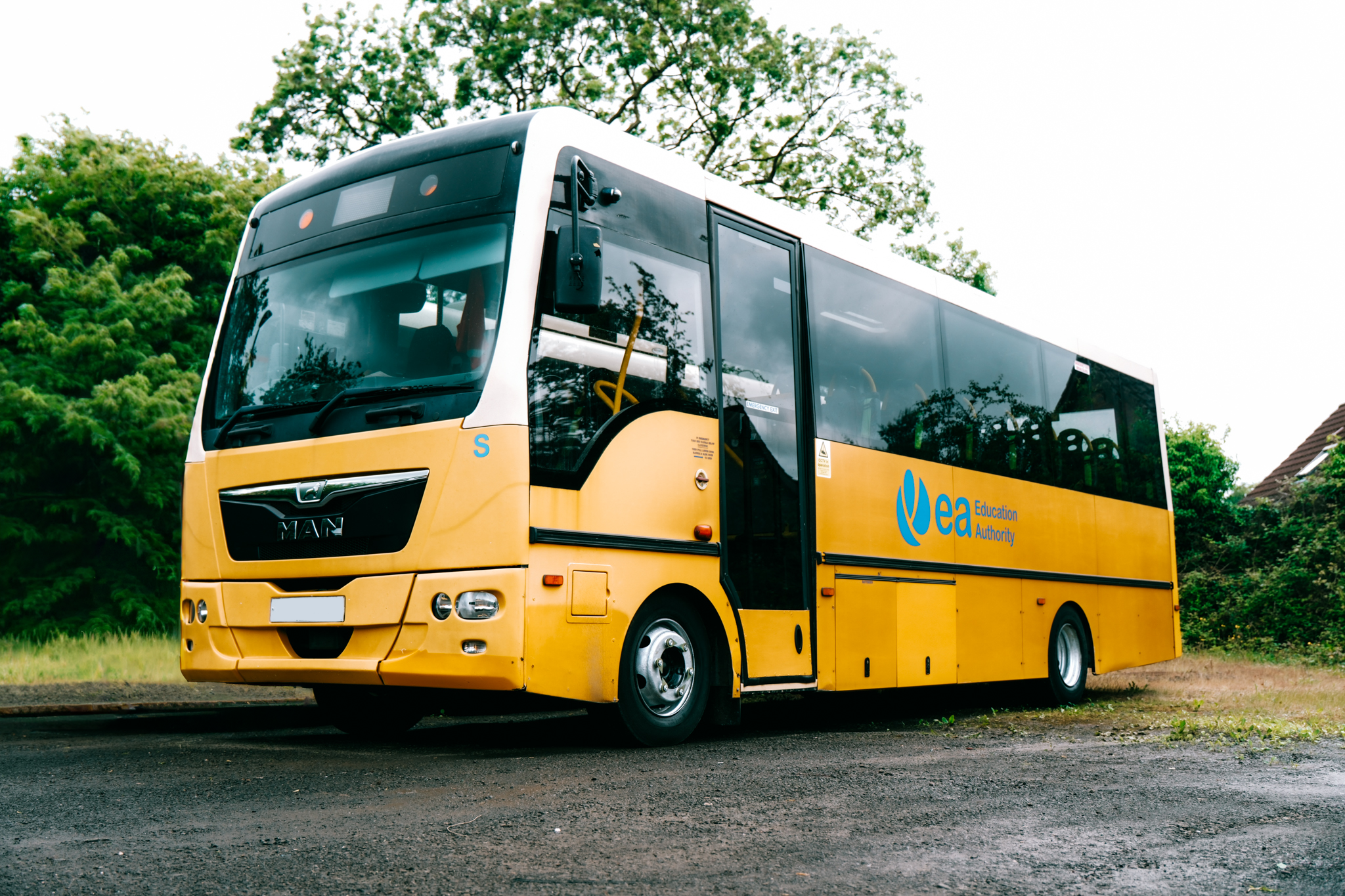 Yellow and black bus with 'Eea Education Authority' logo parked on a road with green trees in the background.