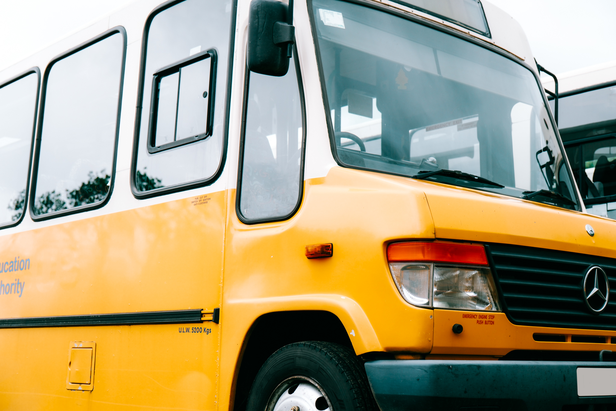 Close-up of a yellow and white Mercedes-Benz bus showing the front and side, including the windshield, side mirror, headlight, and part of the door.