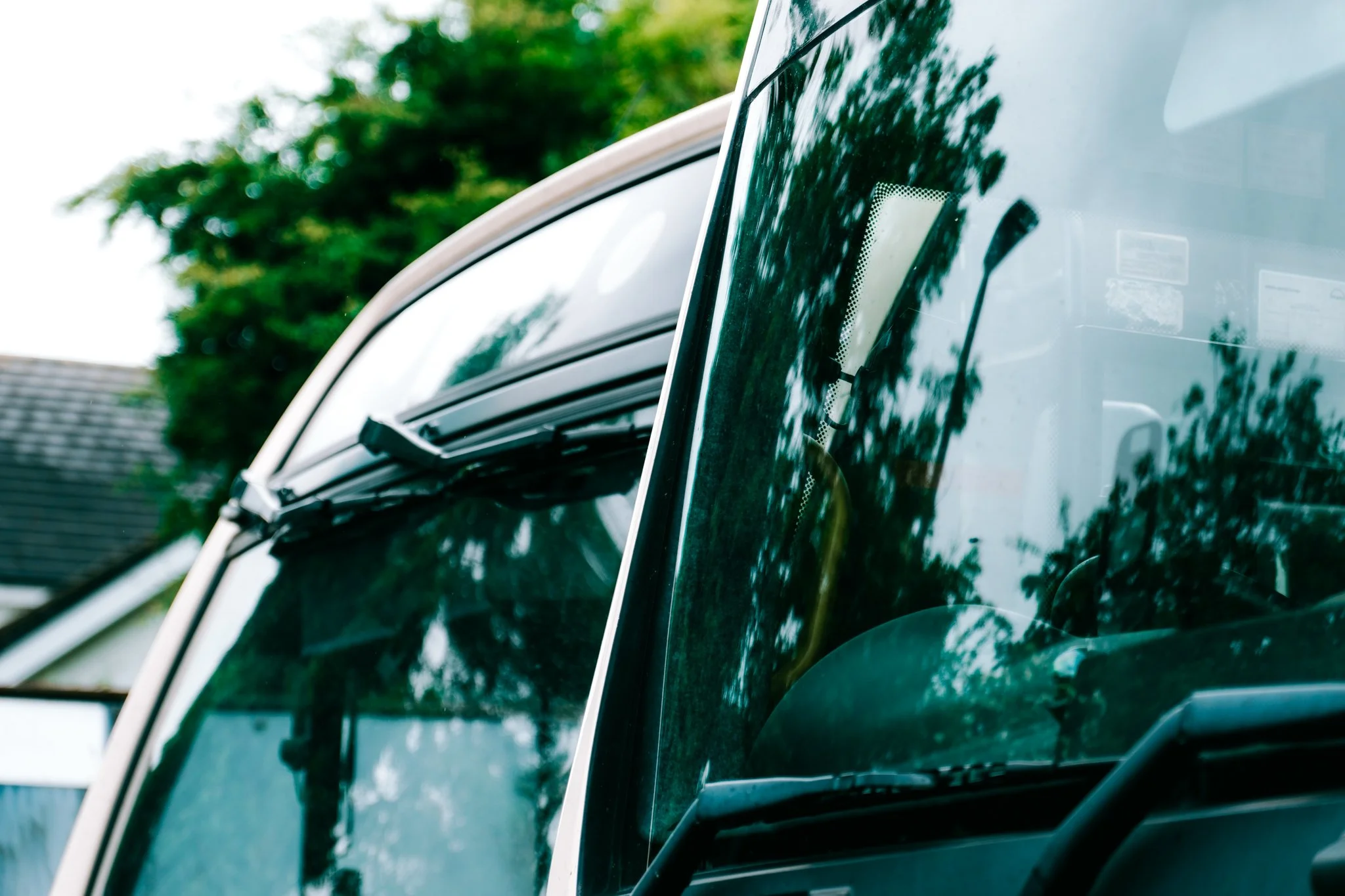 Close-up of a dark green vehicle's windshield with reflections of trees and a streetlight.