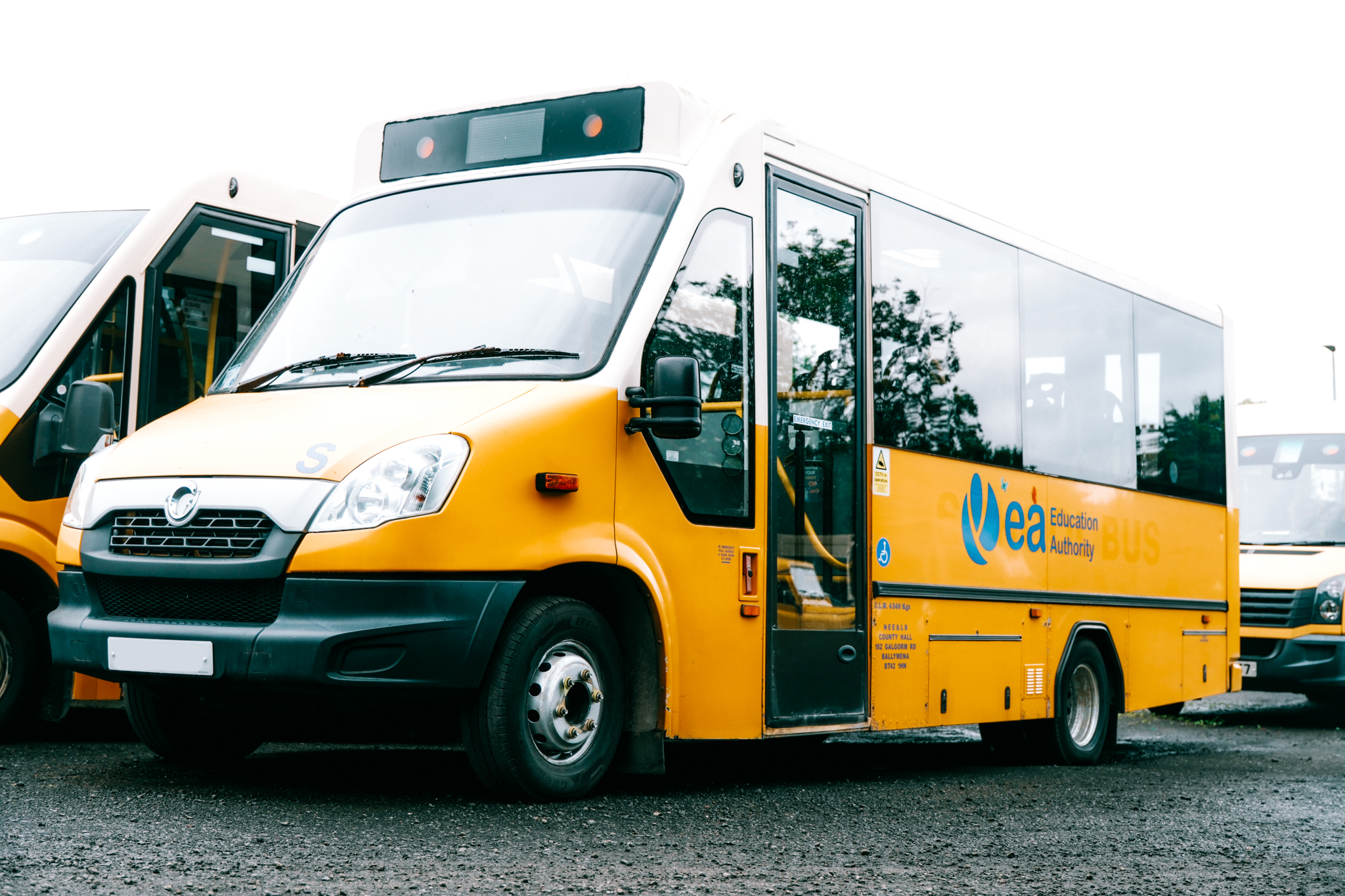 Yellow skirted bus with 'EAA Education Authority' logo parked among other buses on a gravel lot.