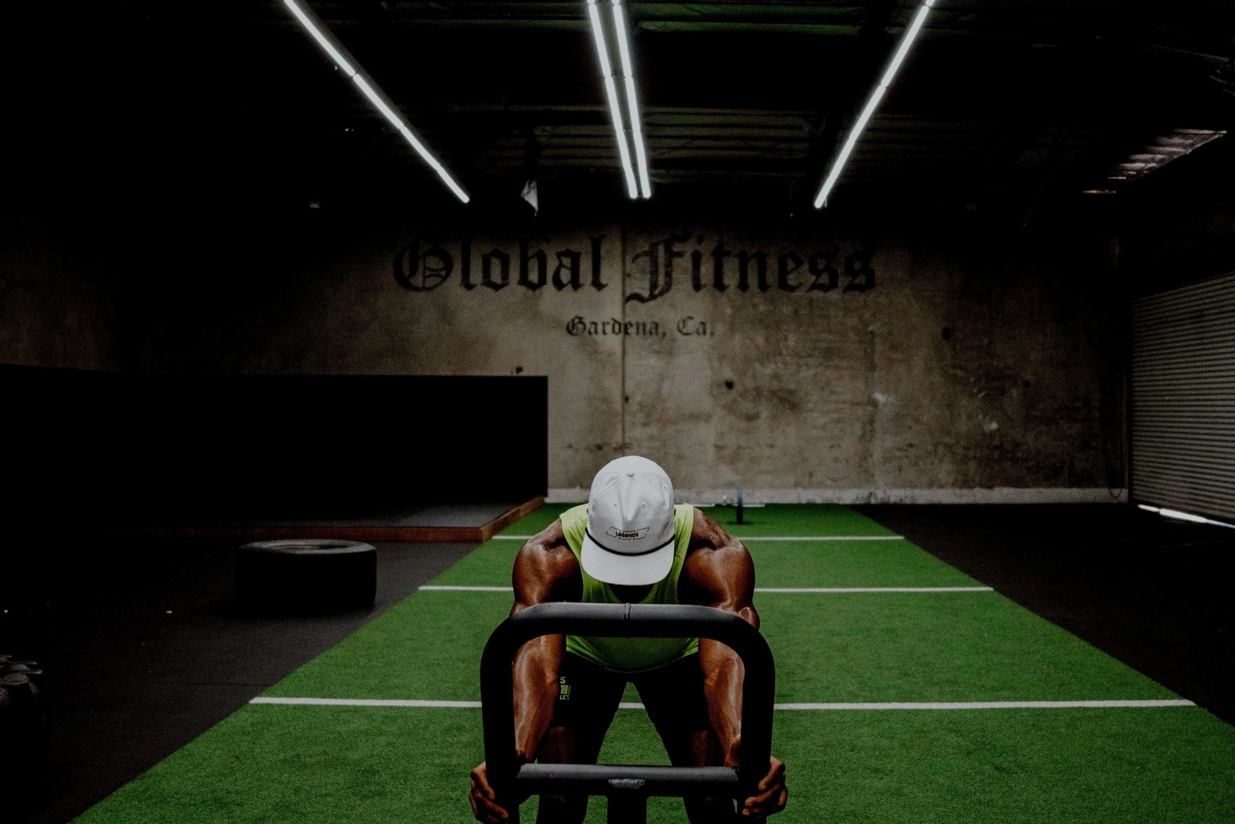 A man exercising with a sled push at Global Fitness gym in Gardena, California, with artificial turf flooring.