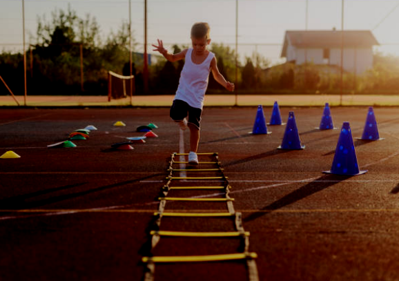 Child running through agility training equipment on an outdoor sports court during sunset.