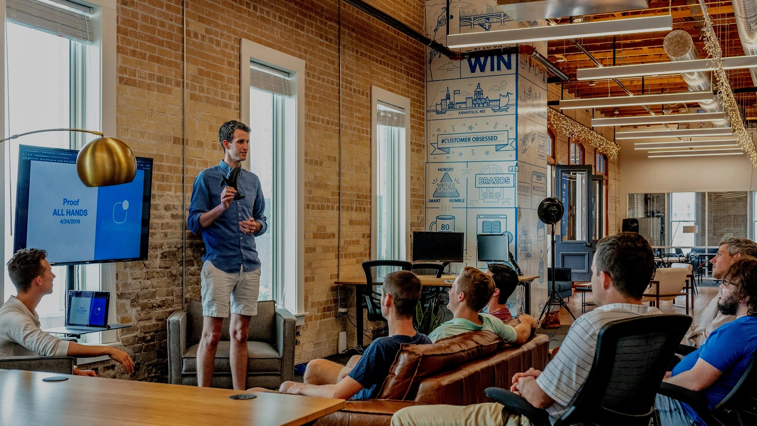 A man giving a presentation in an office space with several people seated and listening.