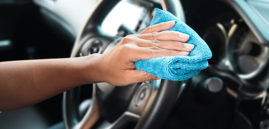 Person cleaning the steering wheel of a car with a blue microfiber cloth.