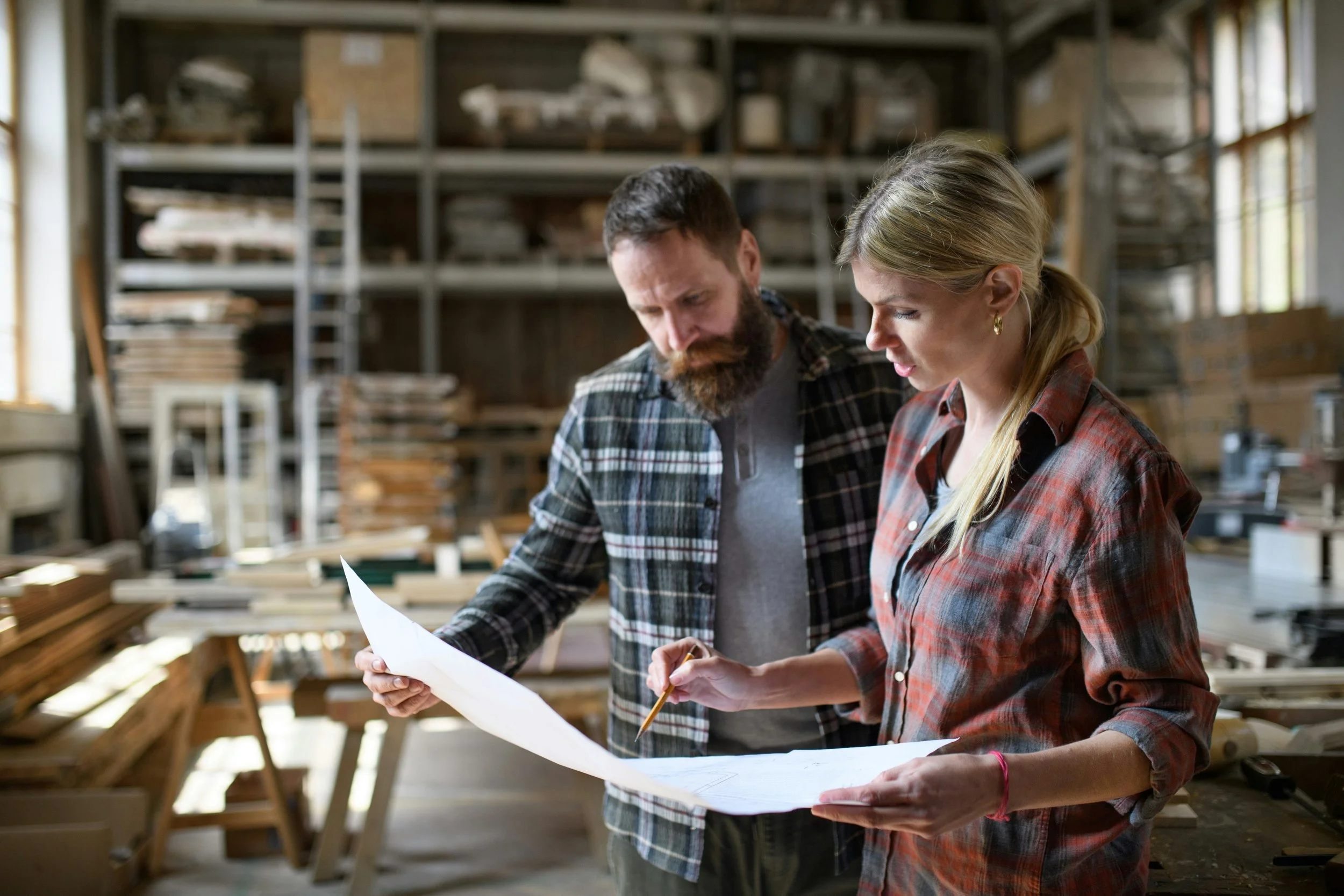 A man and woman inspecting blueprints in a woodworking shop.
