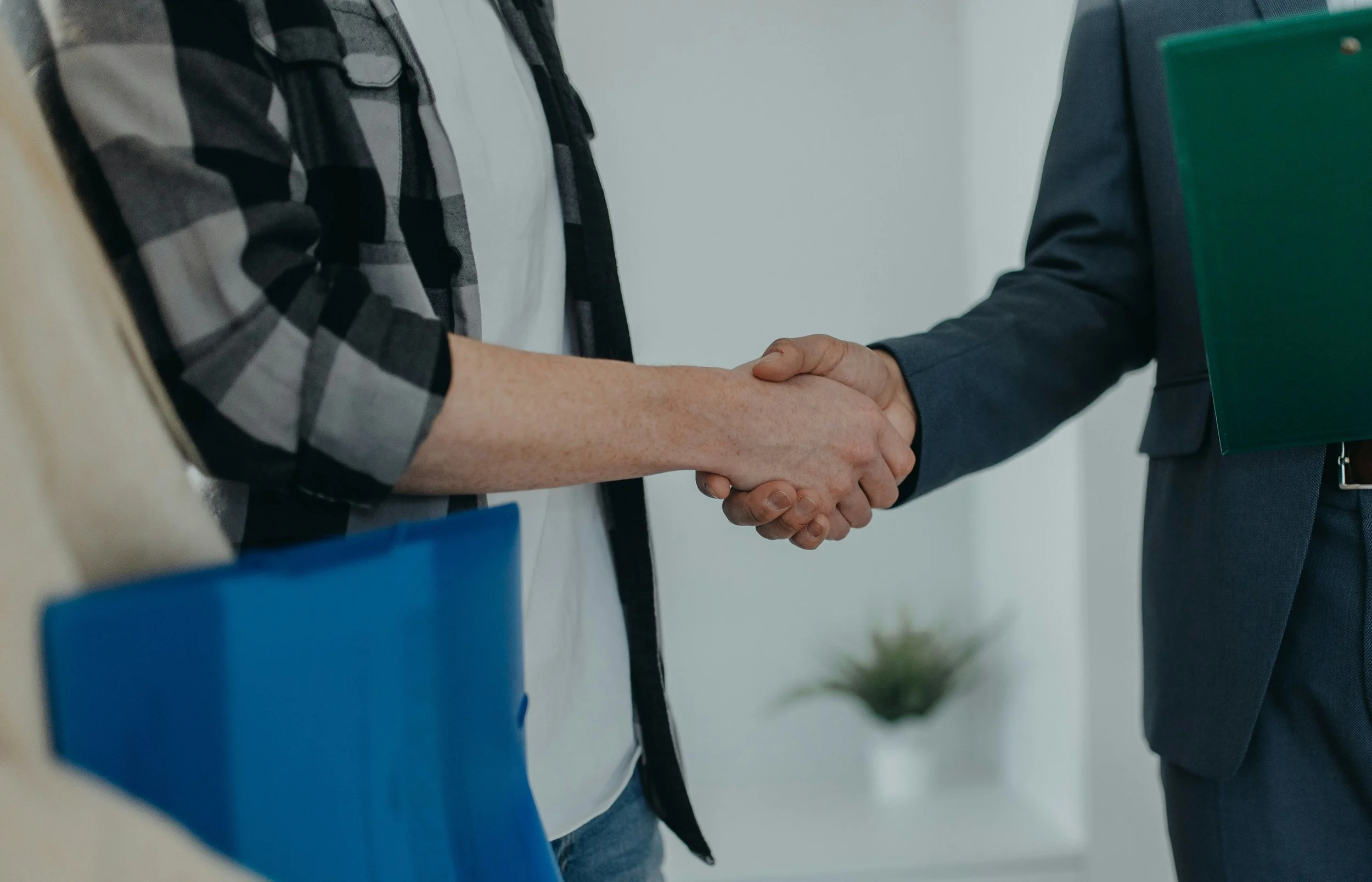 Two people shaking hands during a meeting or agreement, with one person holding a folder.