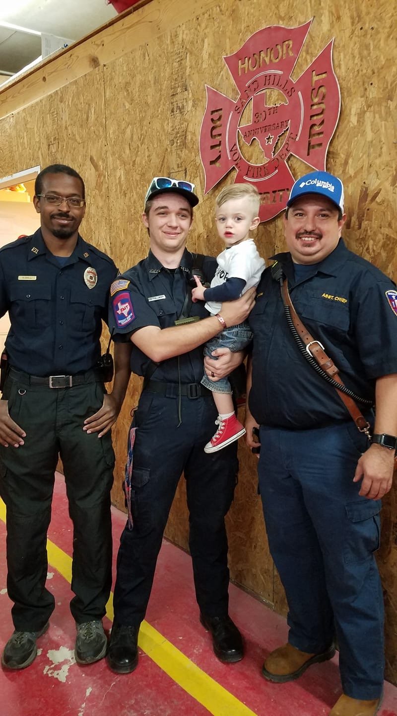 Photo of Hamza Ball, KB Hallmark V, and Carlos Chapa after a ceremony honoring the three for a successful save of a child drowning. Pictured being held by KB Hallmark V, is Luke Bright, who was saved.