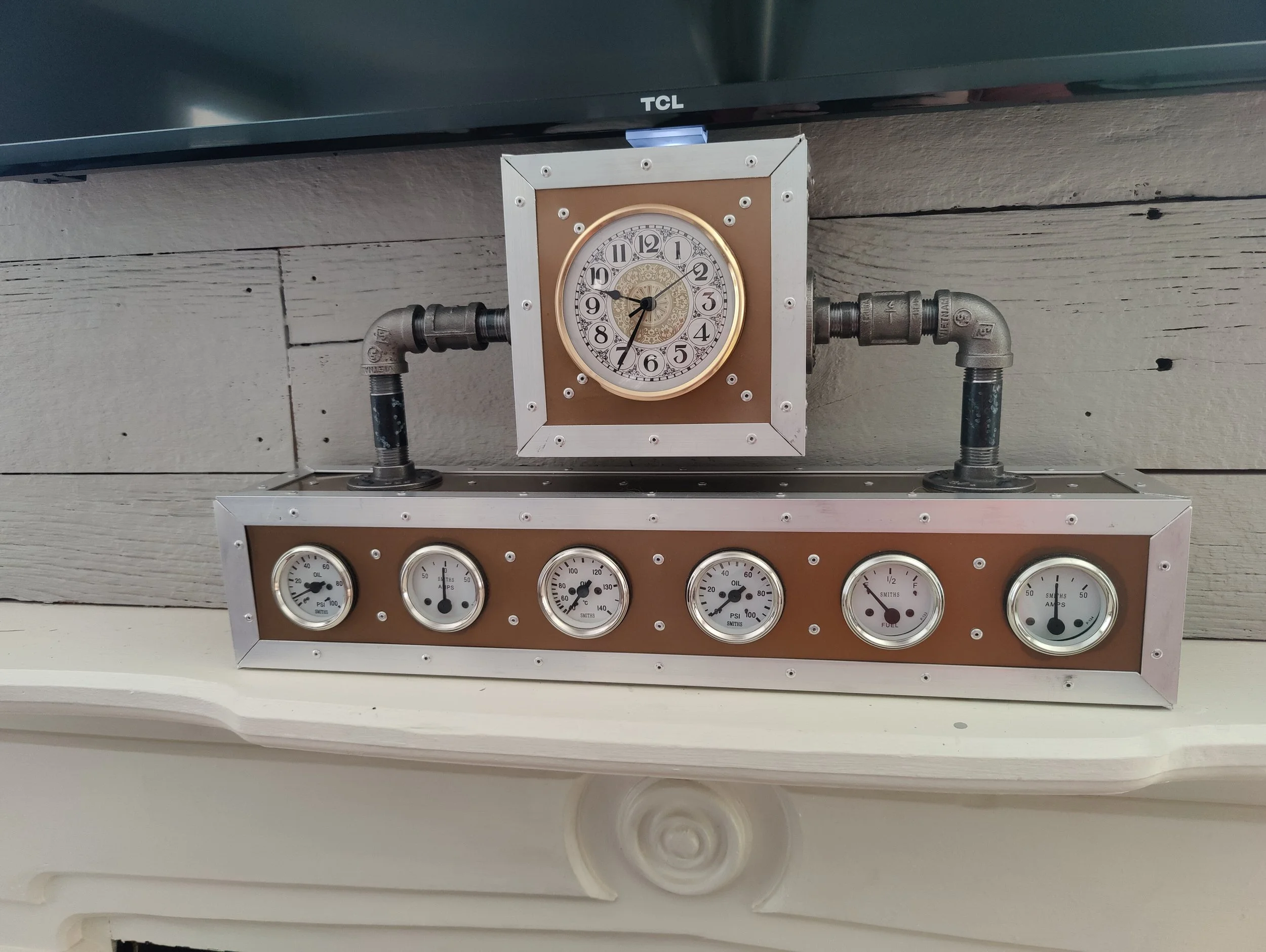 Decorative clock with industrial pipes and gauges mounted on a wooden wall.