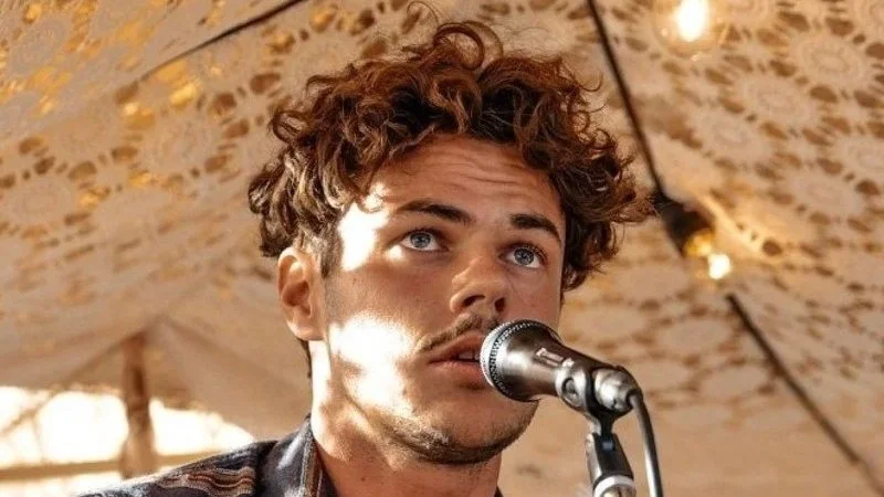 Oly Sherman looking on as he sings into a microphone.