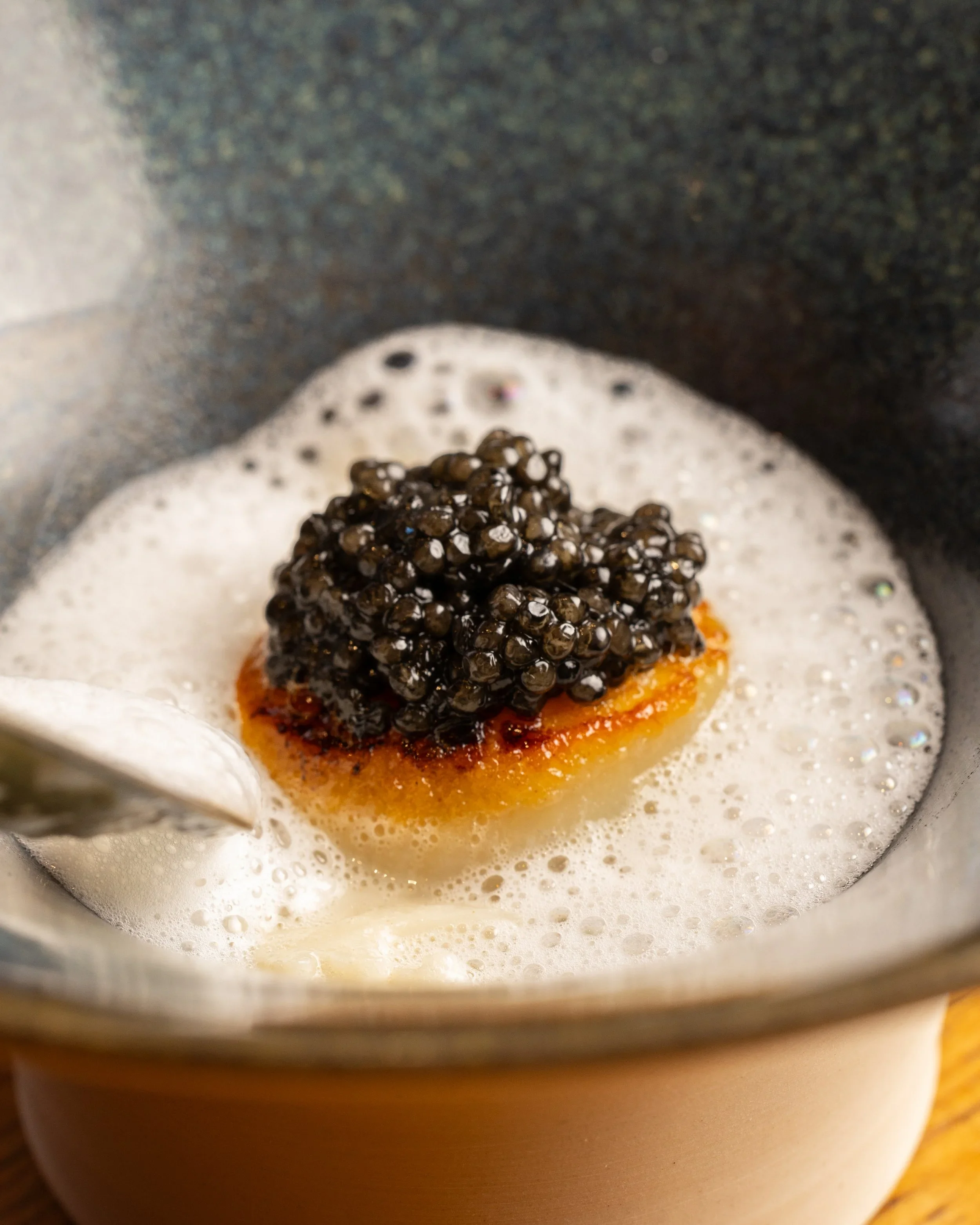 Close-up of a blackberry-topped dessert with orange sauce and foamy cream on a plate