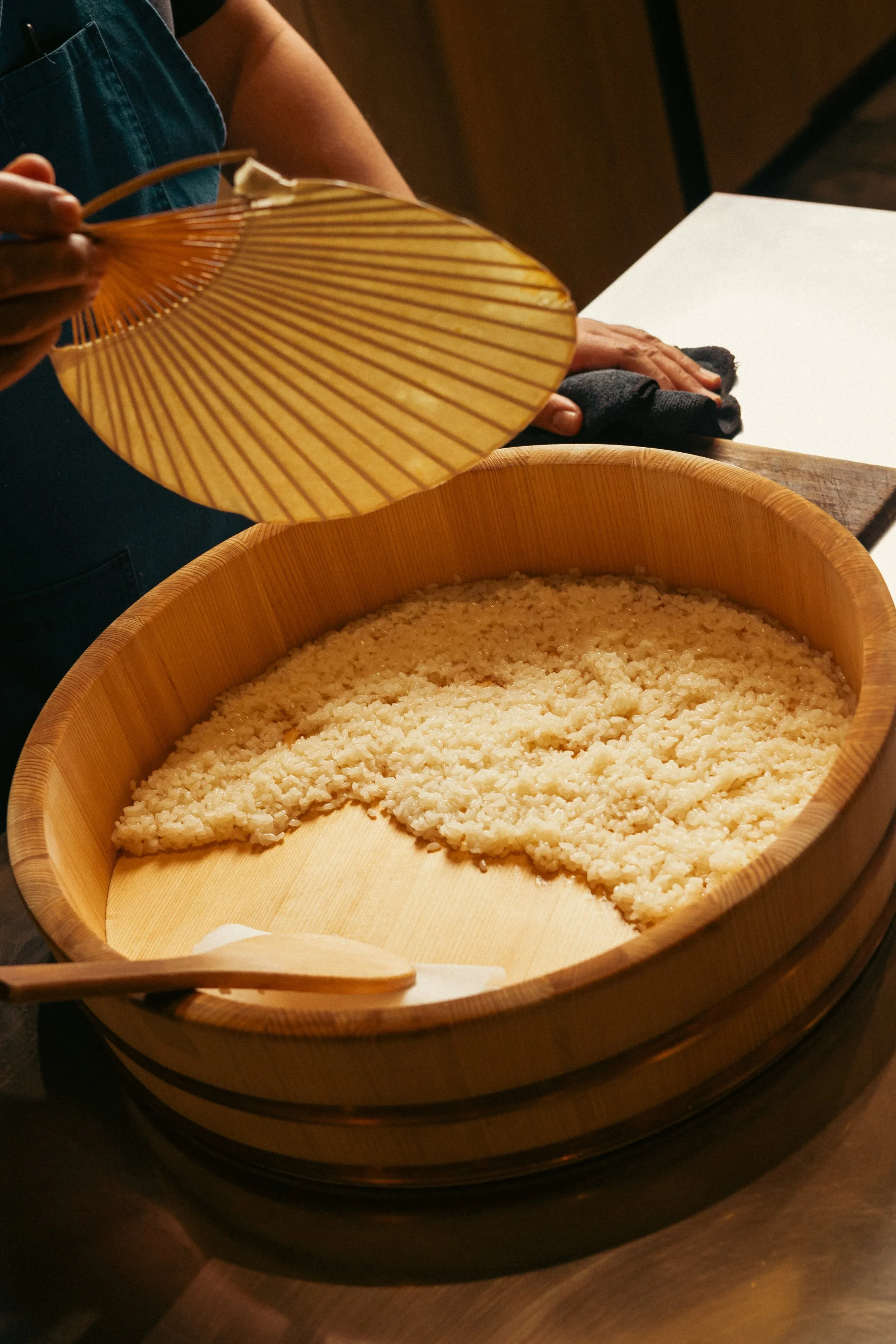 Person using a wooden rice paddle to serve steamed rice from a traditional wooden rice tub.