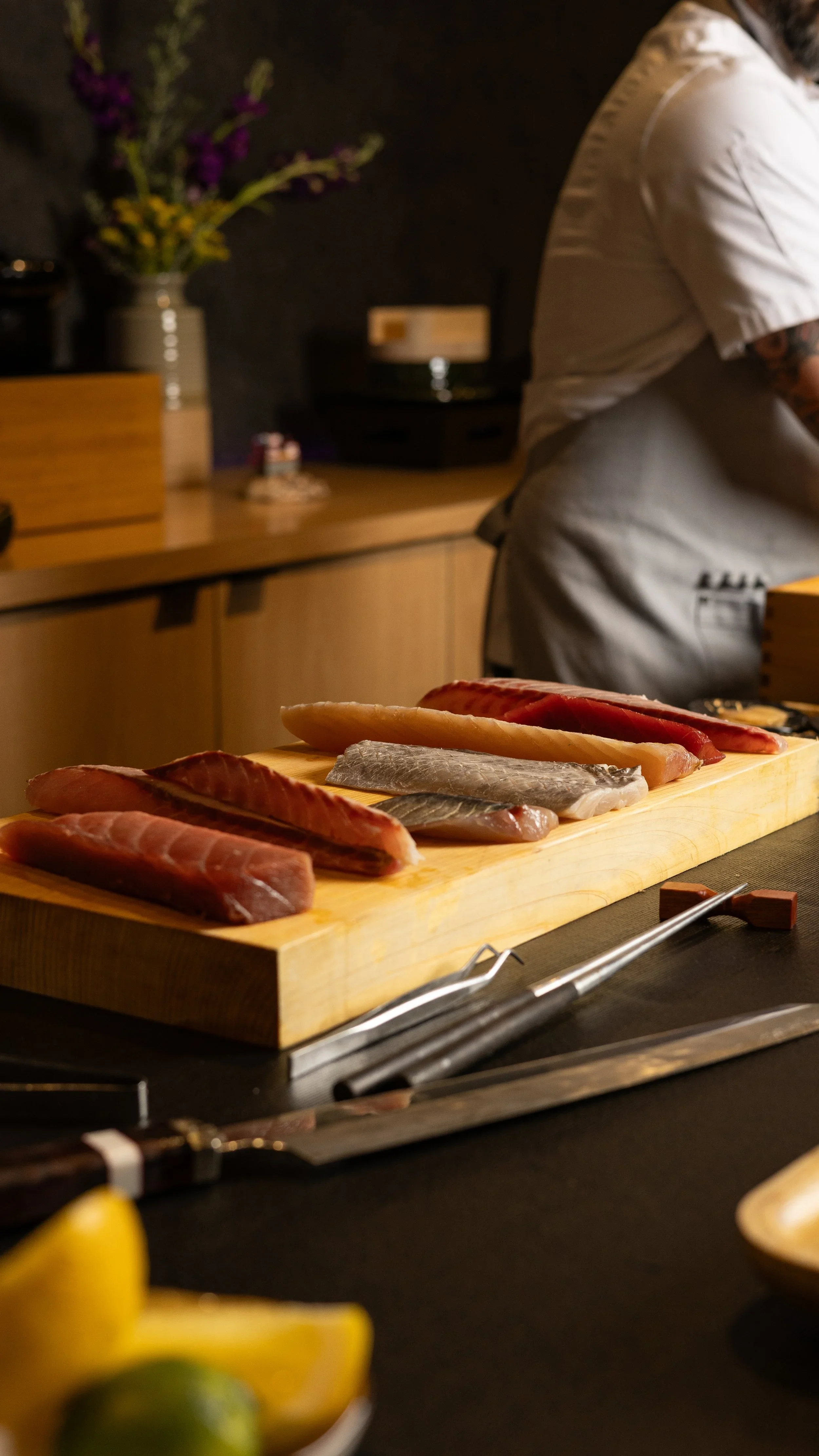 Chef Michael Collantes preparing fish for omakase on a wooden cutting board