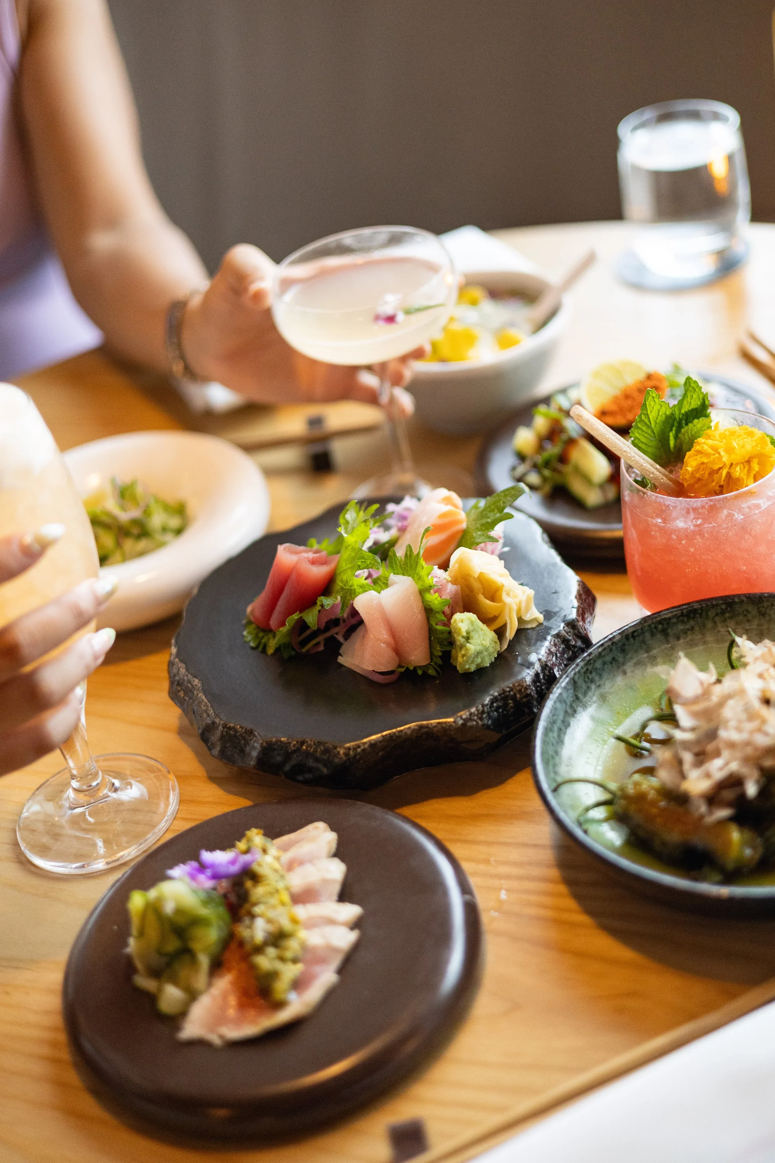 Diners enjoying an upscale meal with sushi, colorful dishes, cocktails, and wine at a restaurant table