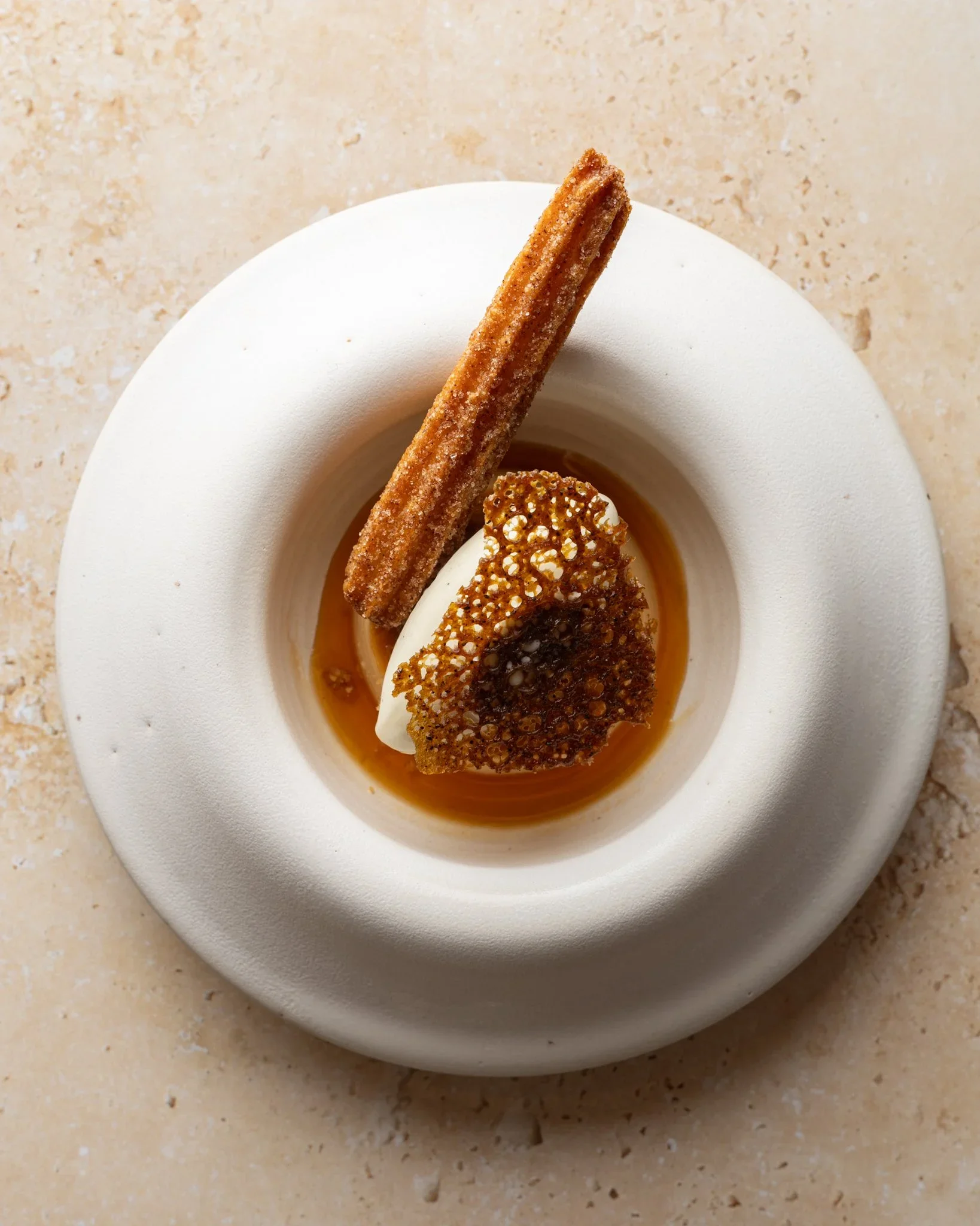 Gourmet dessert with a cinnamon-sugar churro, vanilla ice cream, and caramelized crisp topping in caramel sauce