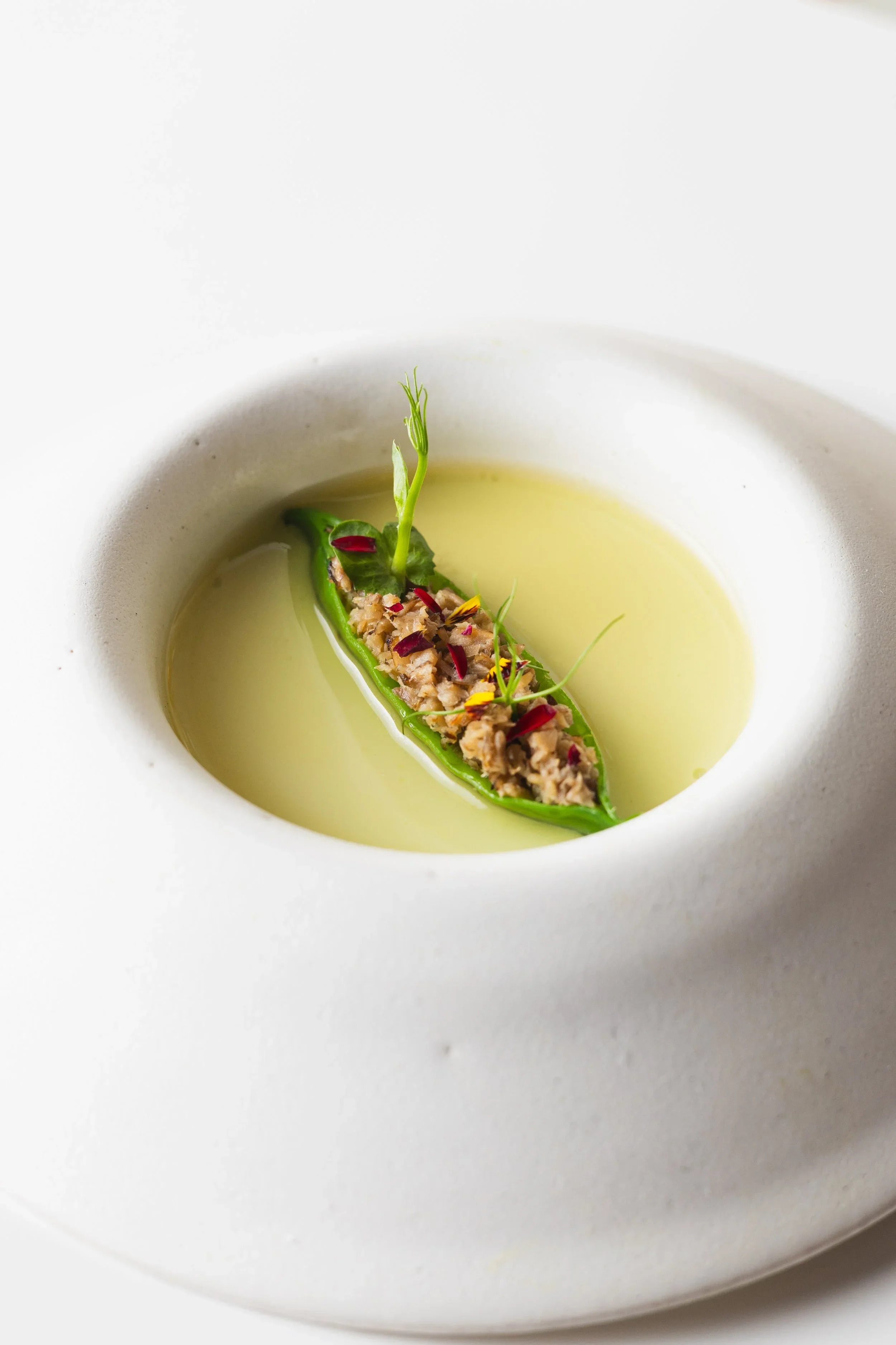 Gourmet dish with minced meat, herbs, edible flowers, and red pepper flakes in a pale broth
