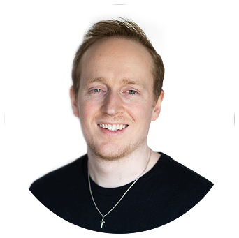 Headshot of a smiling man with short light brown hair, light complexion, wearing a black shirt and a silver necklace with a cross pendant facing the camera