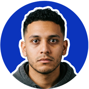 Close-up portrait of a young man with short curly hair, dark eyes, and a serious expression, wearing a dark hoodie against a blue background.