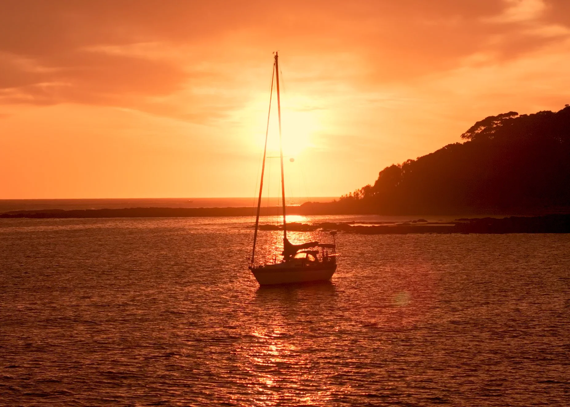 Sailboat on calm water at sunset with a hillside in the background