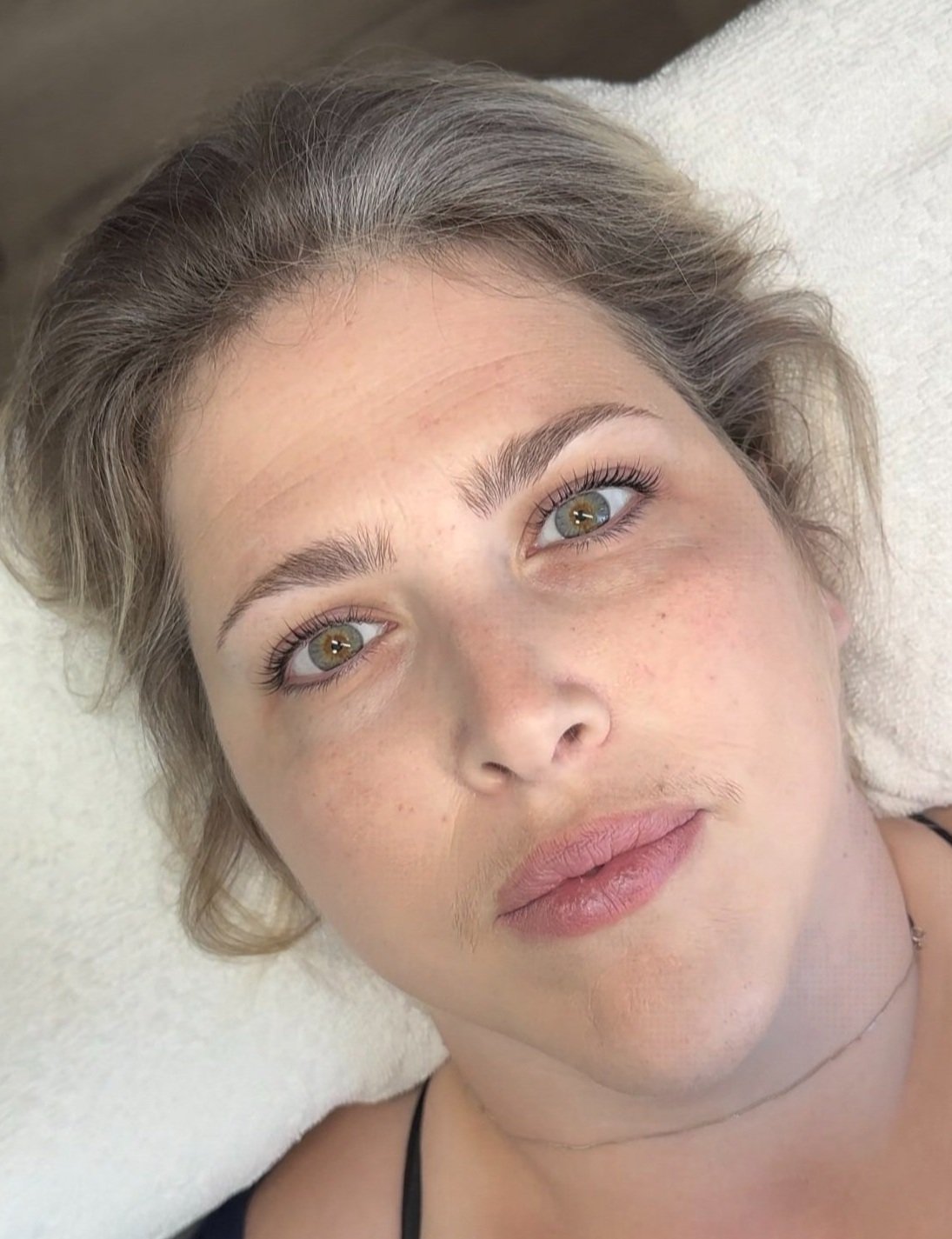 Close-up of a woman with light brown hair, hazel eyes, and freckles, lying on a white surface.