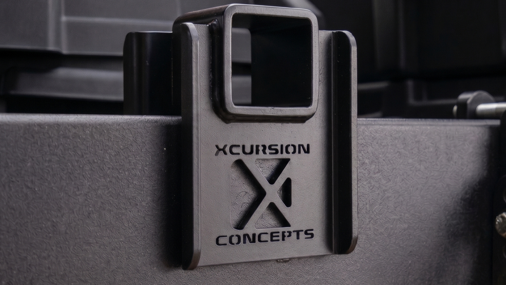 XCursion Concepts laser-cut logo on a heavy-duty black powder-coated trailer hitch receiver accessory frame.
