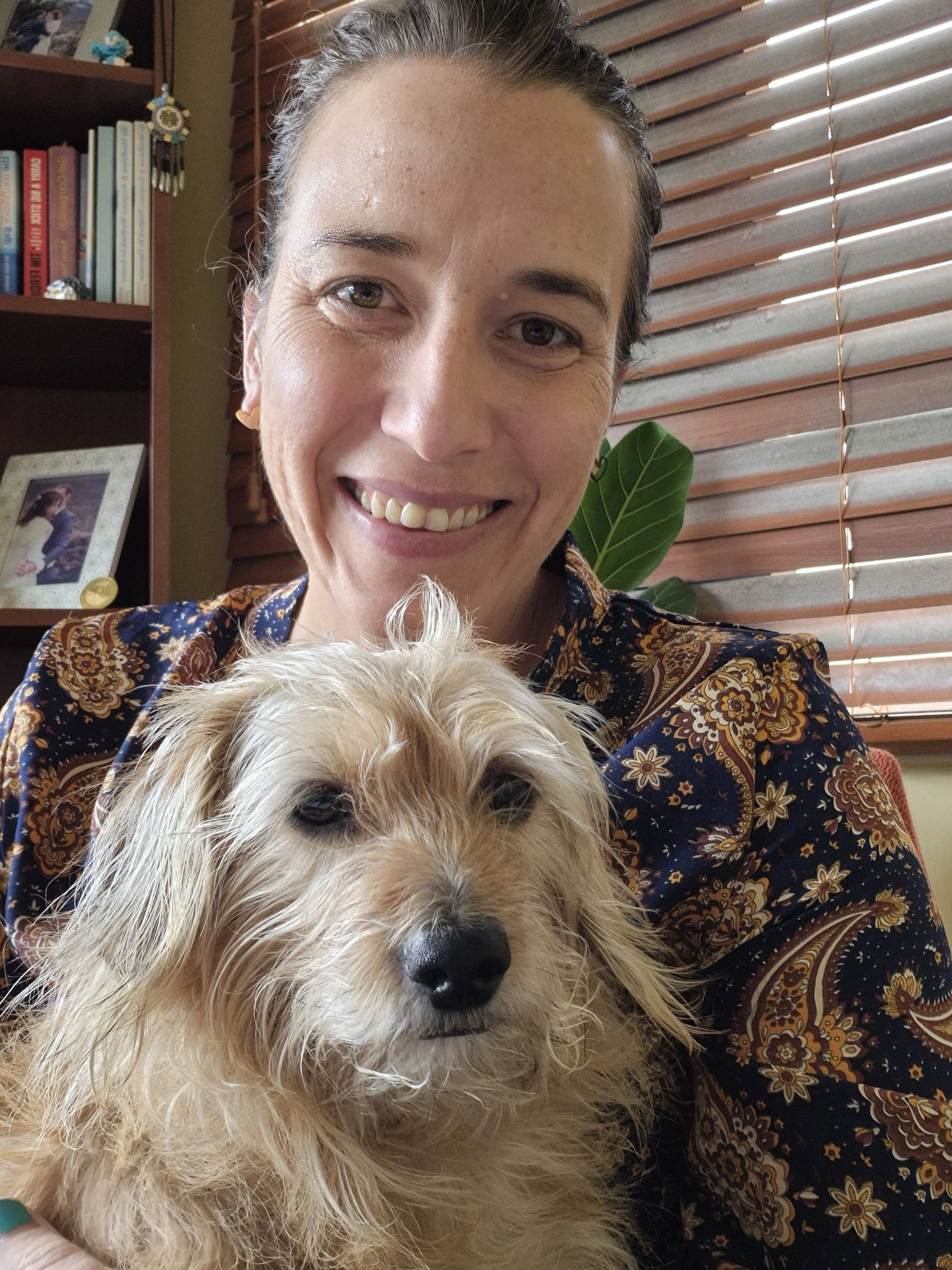 Picture of Shannon A Swales with her dog hana. Behind her is a wooden book shelf and plant