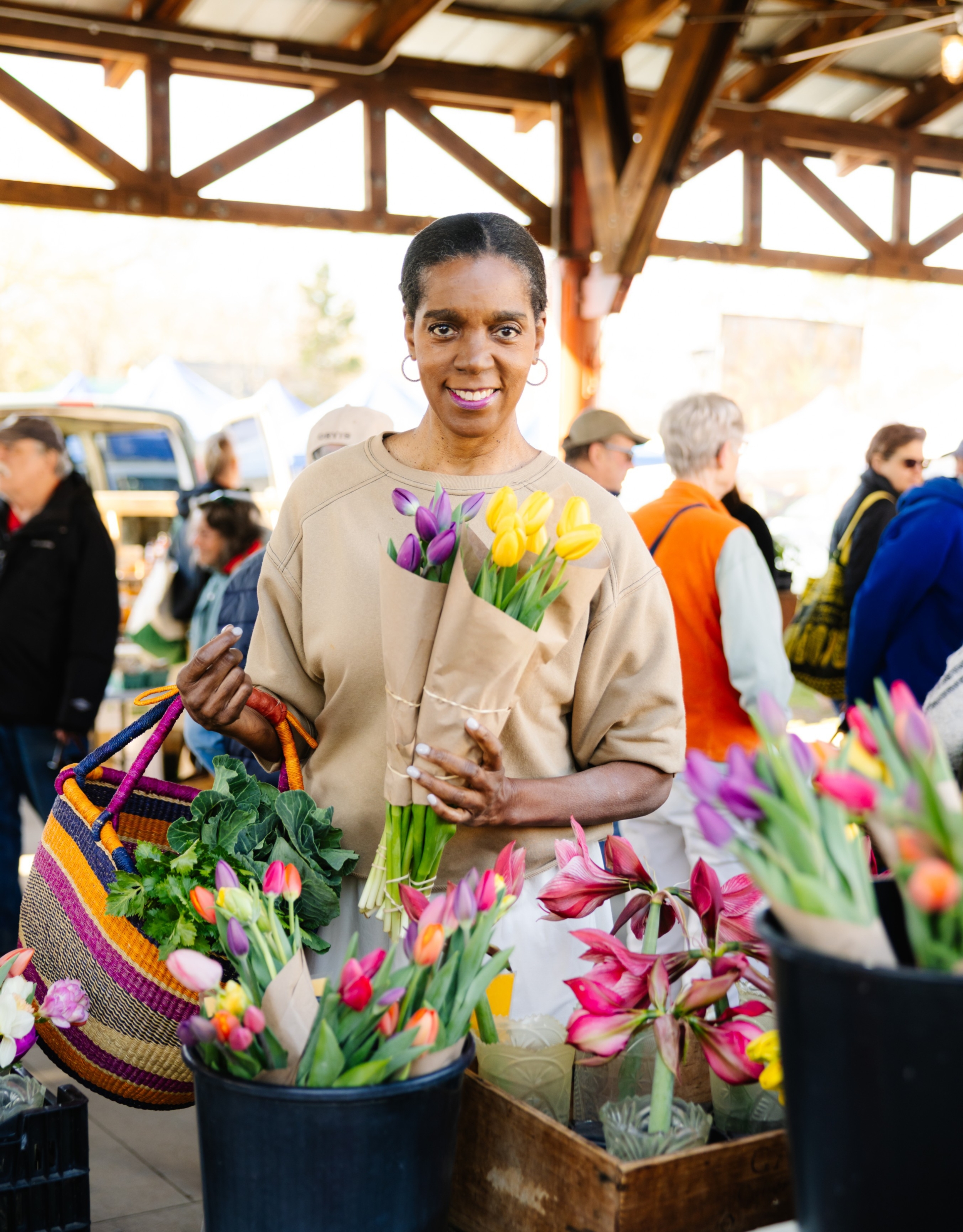 Spring Council holding a beautiful purple and yellow tulips at a local flower farmer's stall at the Carrboro Farmers Market, surrounded by seasonal spring blooms