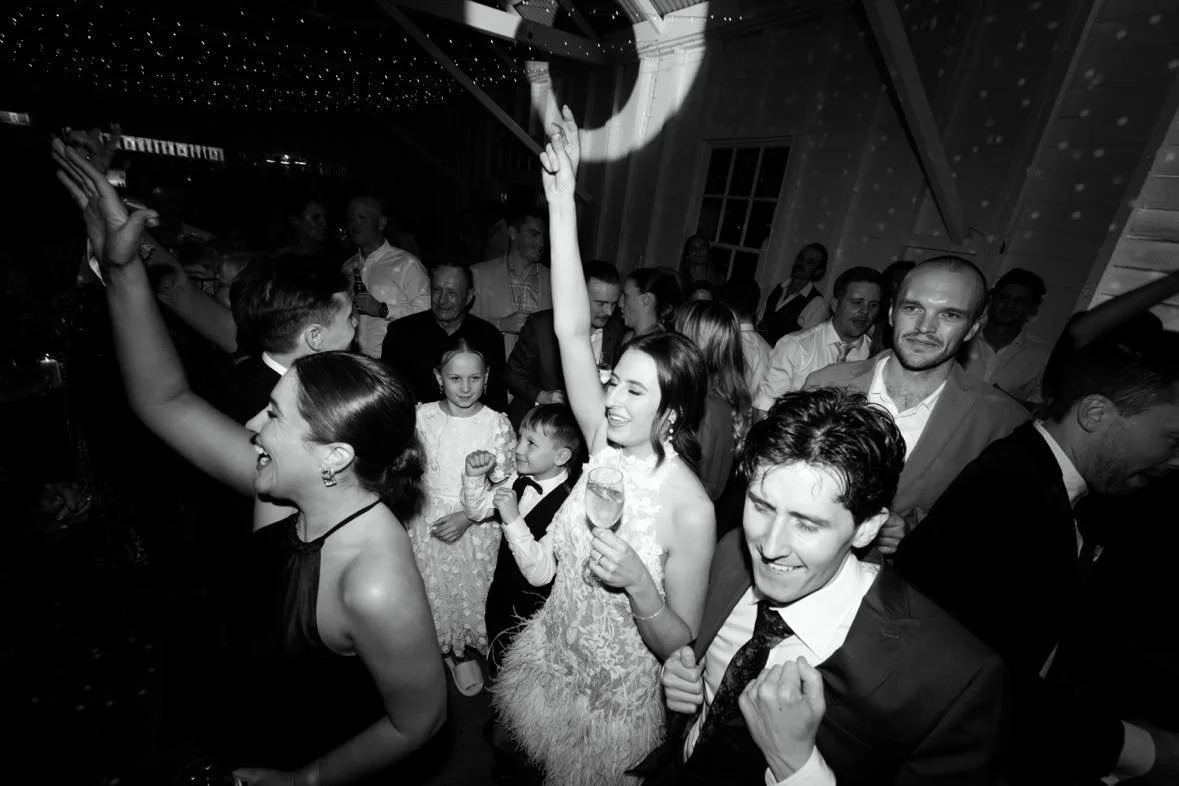 People dancing, smiling, and celebrating at a party or wedding reception in a lively indoor setting.