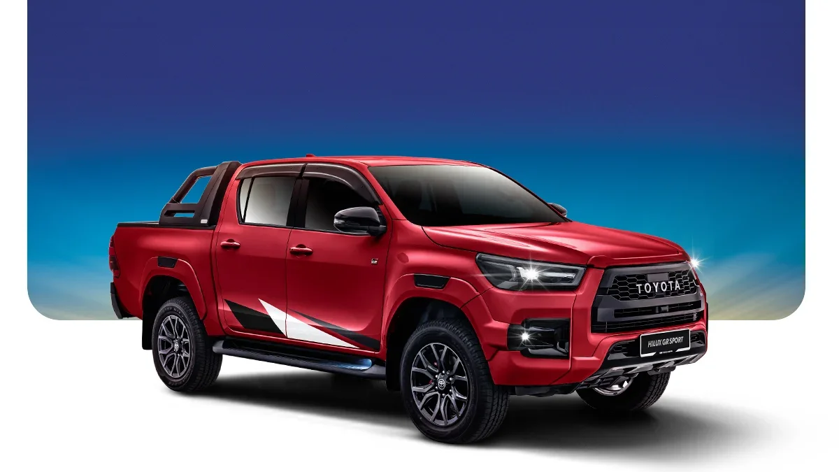 Red Toyota Hilux GR Sport pickup truck with black accents, parked against a gradient blue sky background.