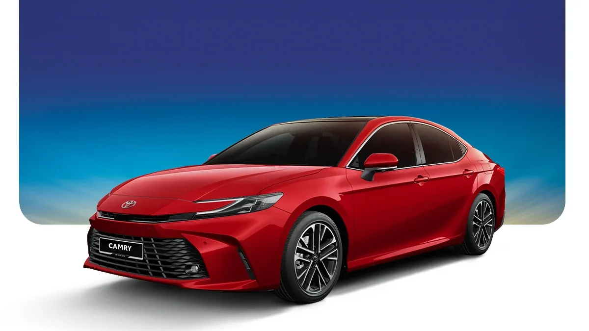 Red Toyota Camry sedan with black tinted windows and black alloy wheels, front view against a gradient blue sky background.