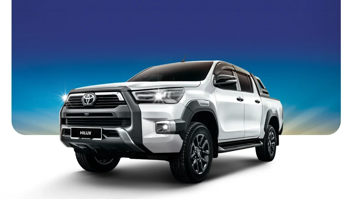 A silver Toyota Hilux pickup truck parked against a gradient sky background, front view with large grille, headlights, and black accents.