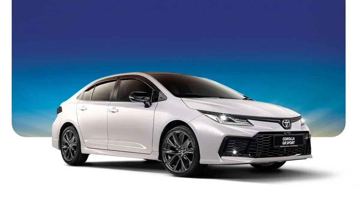 A silver Toyota Corolla GR Sport hatchback car with black wheels, black side mirrors, and a black front grille, against a background of a blue sky with some gradient color.