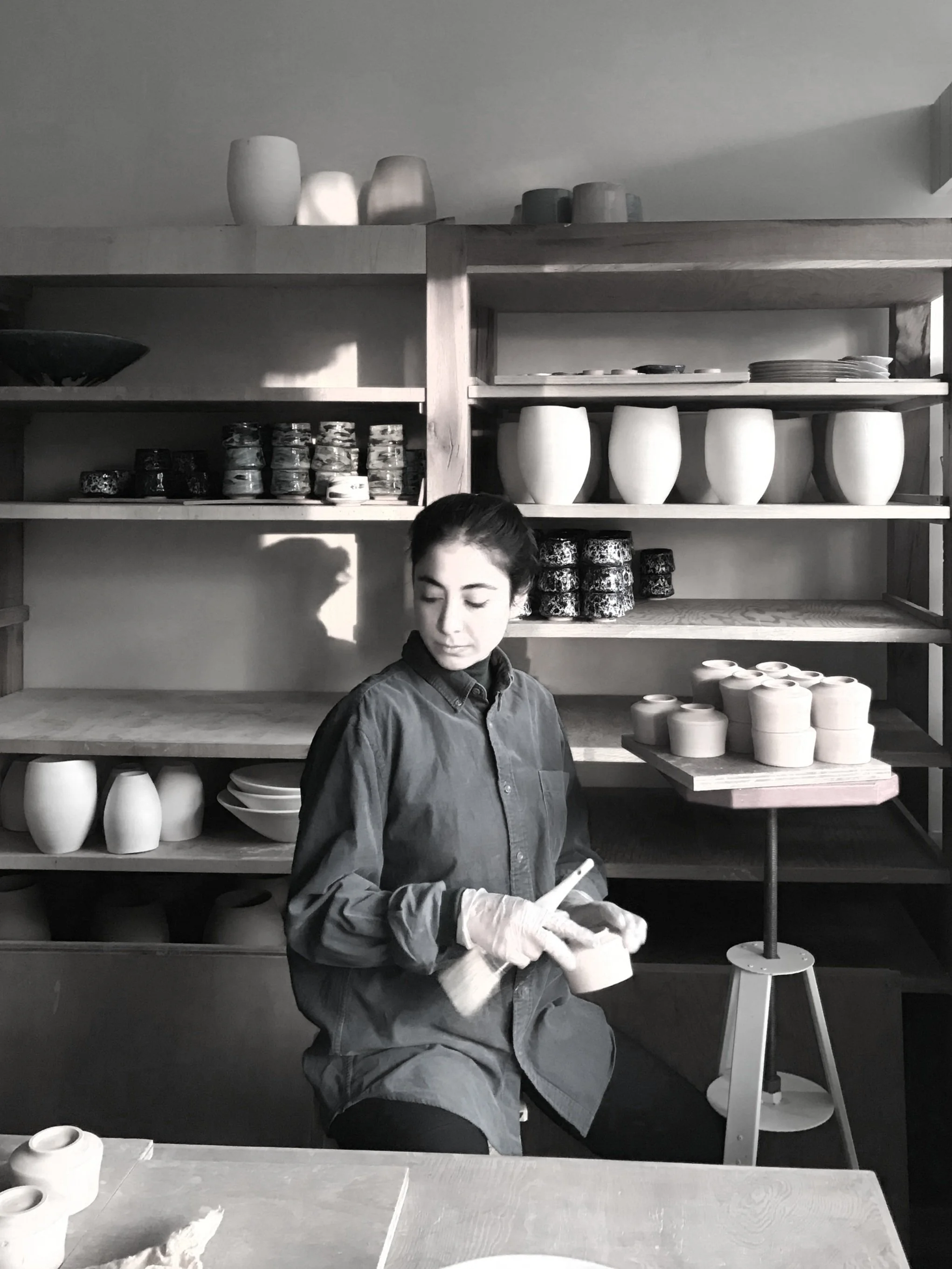 Person working with ceramics, surrounded by pottery on shelves.