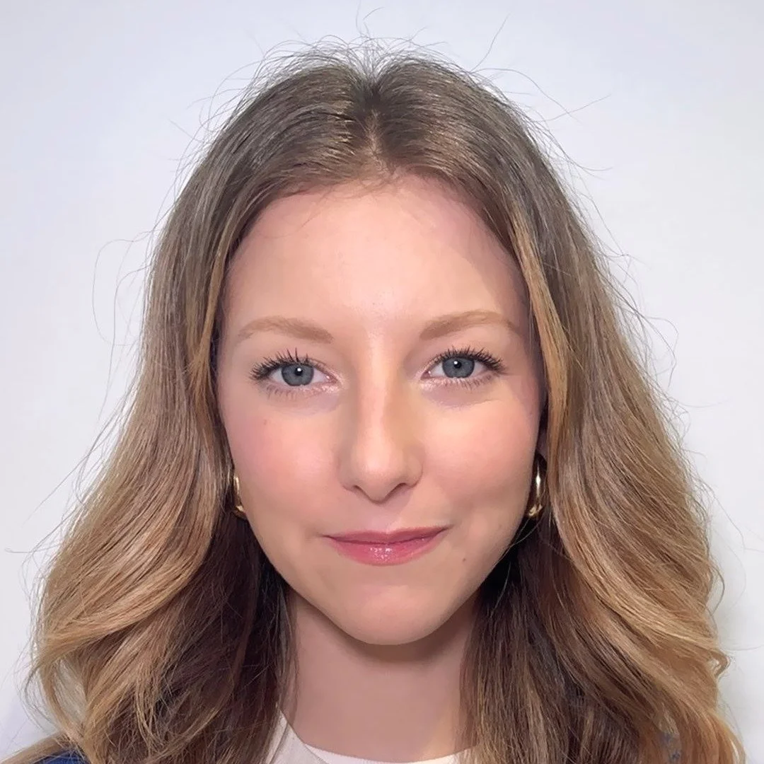 Close-up of a woman with blonde wavy hair, light skin, and blue eyes, smiling gently at the camera.