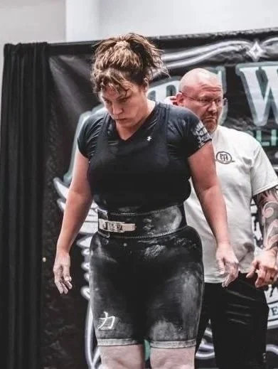 Female powerlifter standing with coach, covered in chalk, at a competition.
