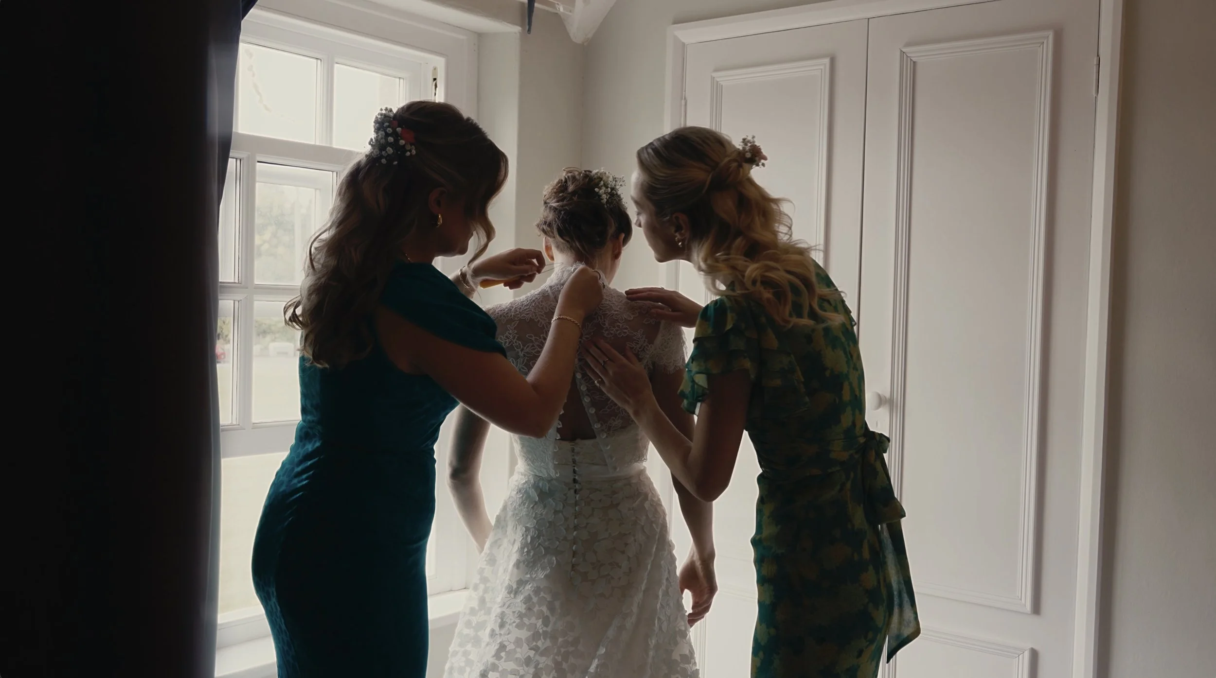 Bridesmaids helping to fasten brides dress