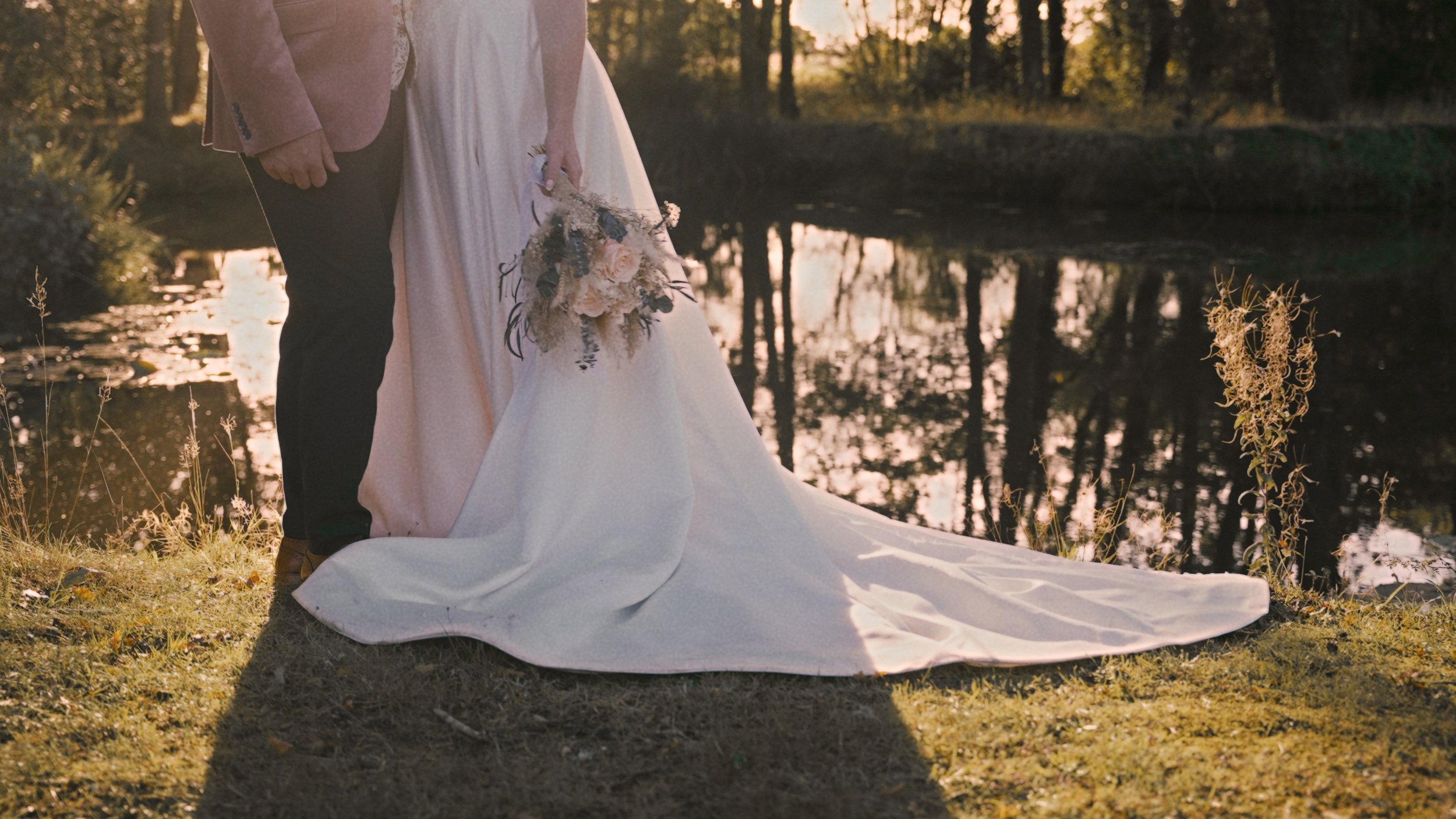 Lower half of bride and grooms body with a lake behind them.