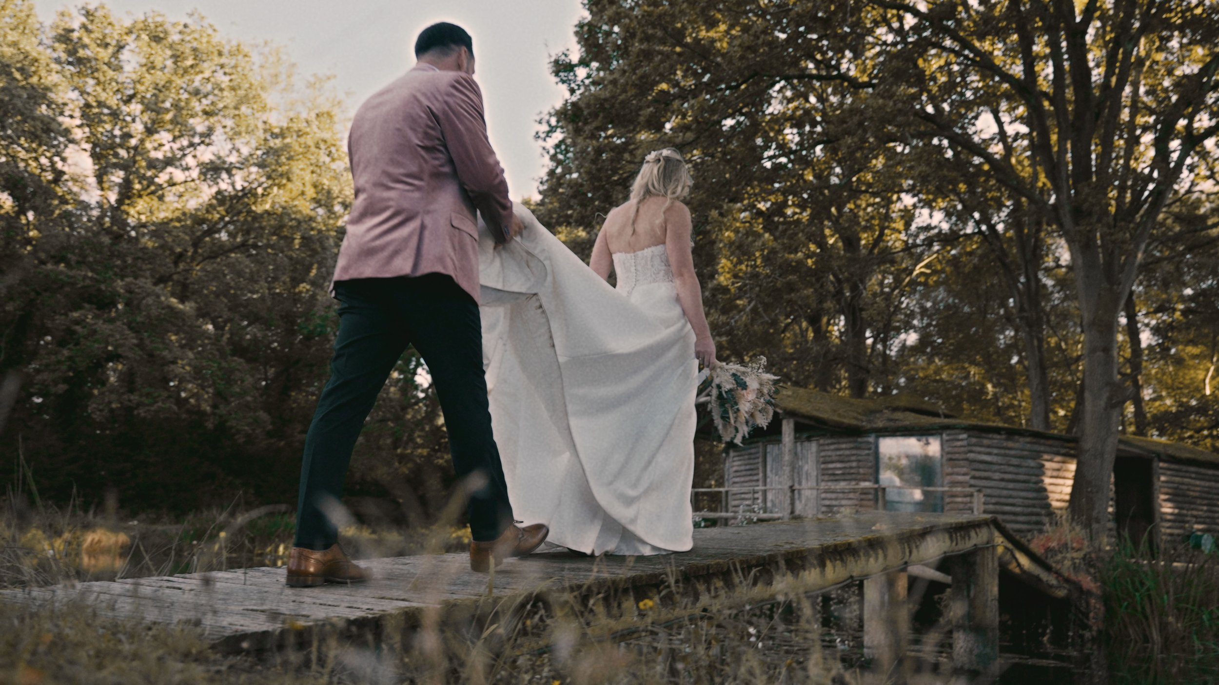 Bride and groom walking over a bridge and groom carrying bride's dress.