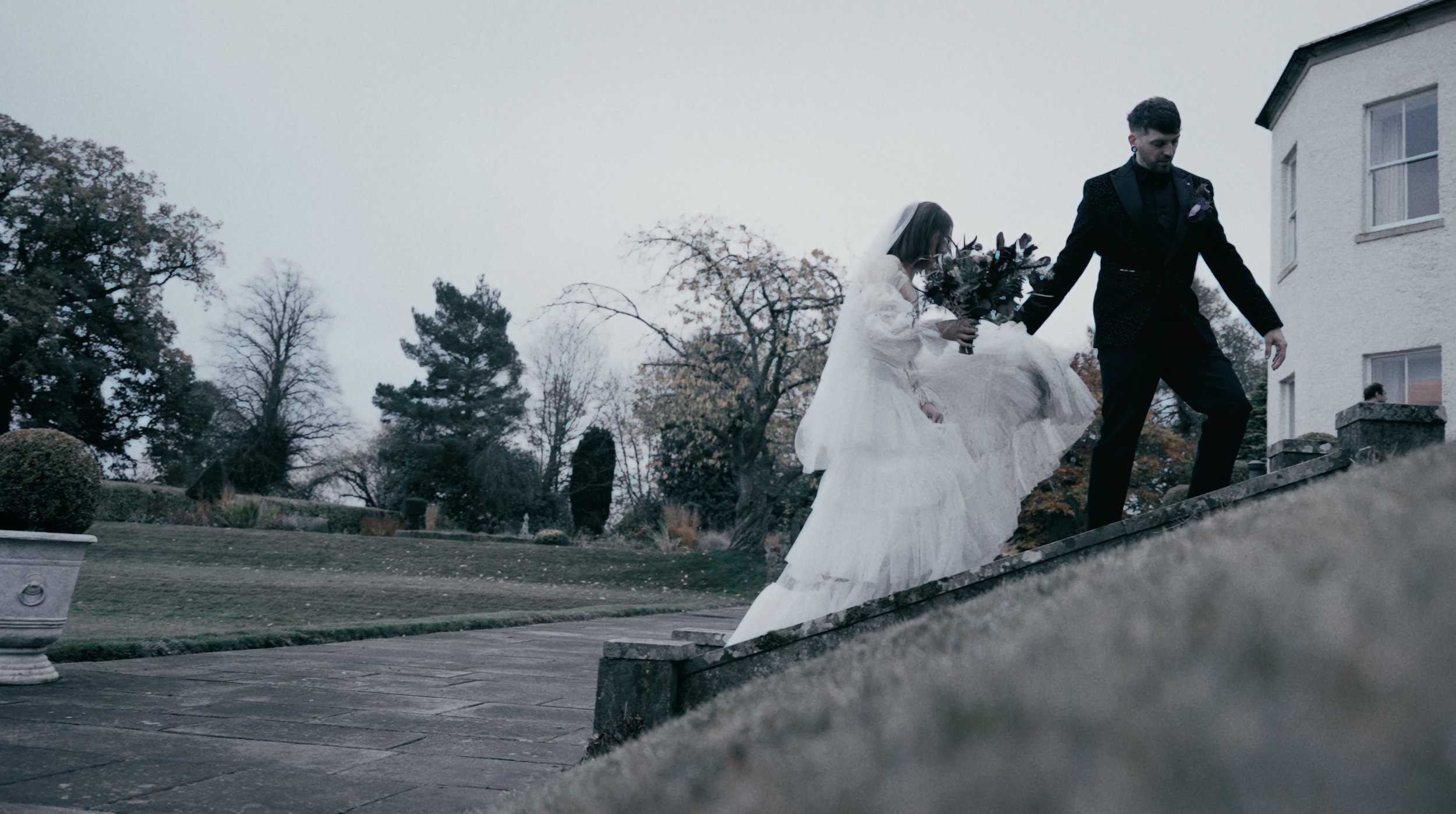 groom helps bride walk up some steps at Lartington Hall